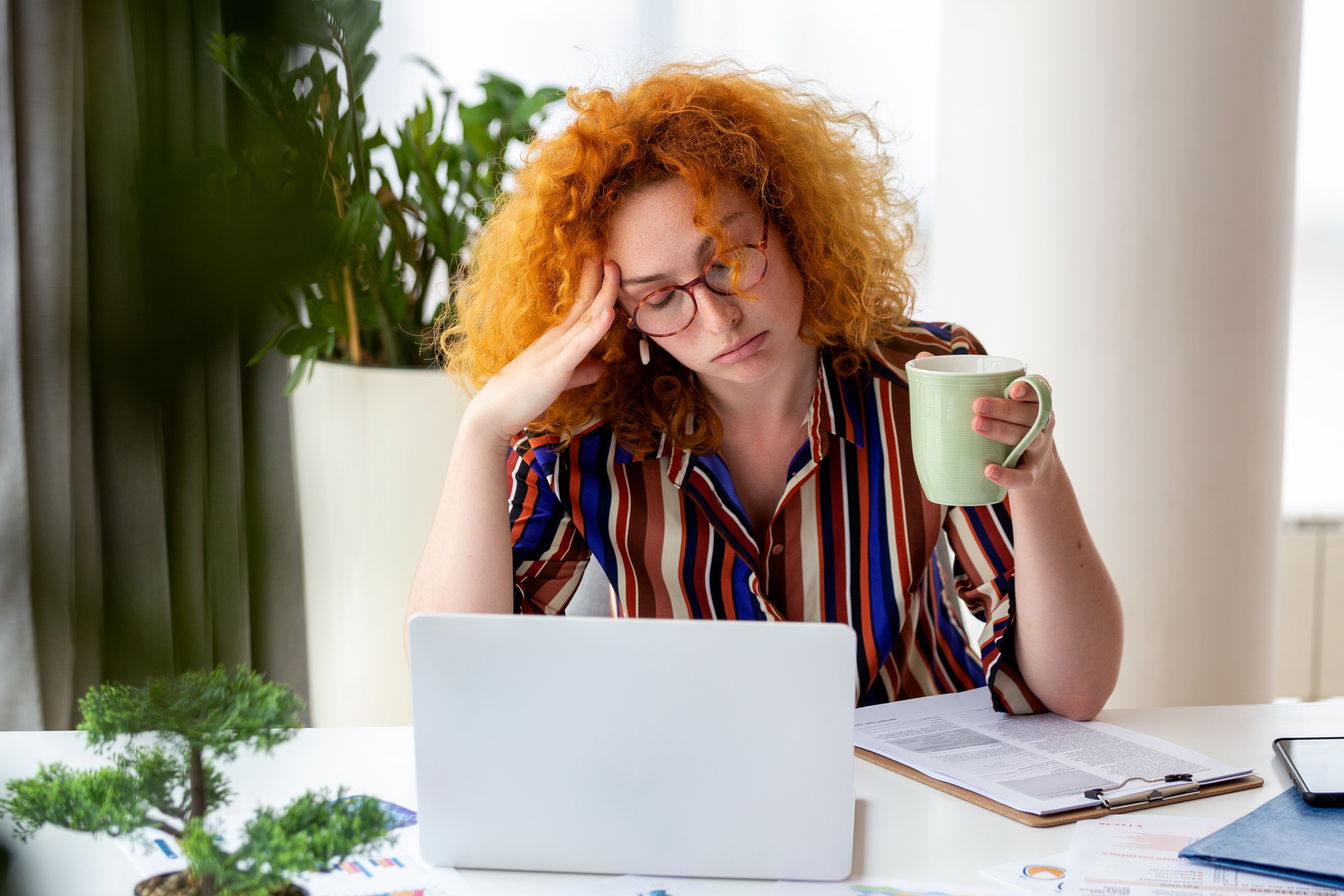Young woman tired, burnout, exhausted from working studying hard. Bored and frustrated. Head resting on hand. Bright space big windows. At home concept. Stress concept.