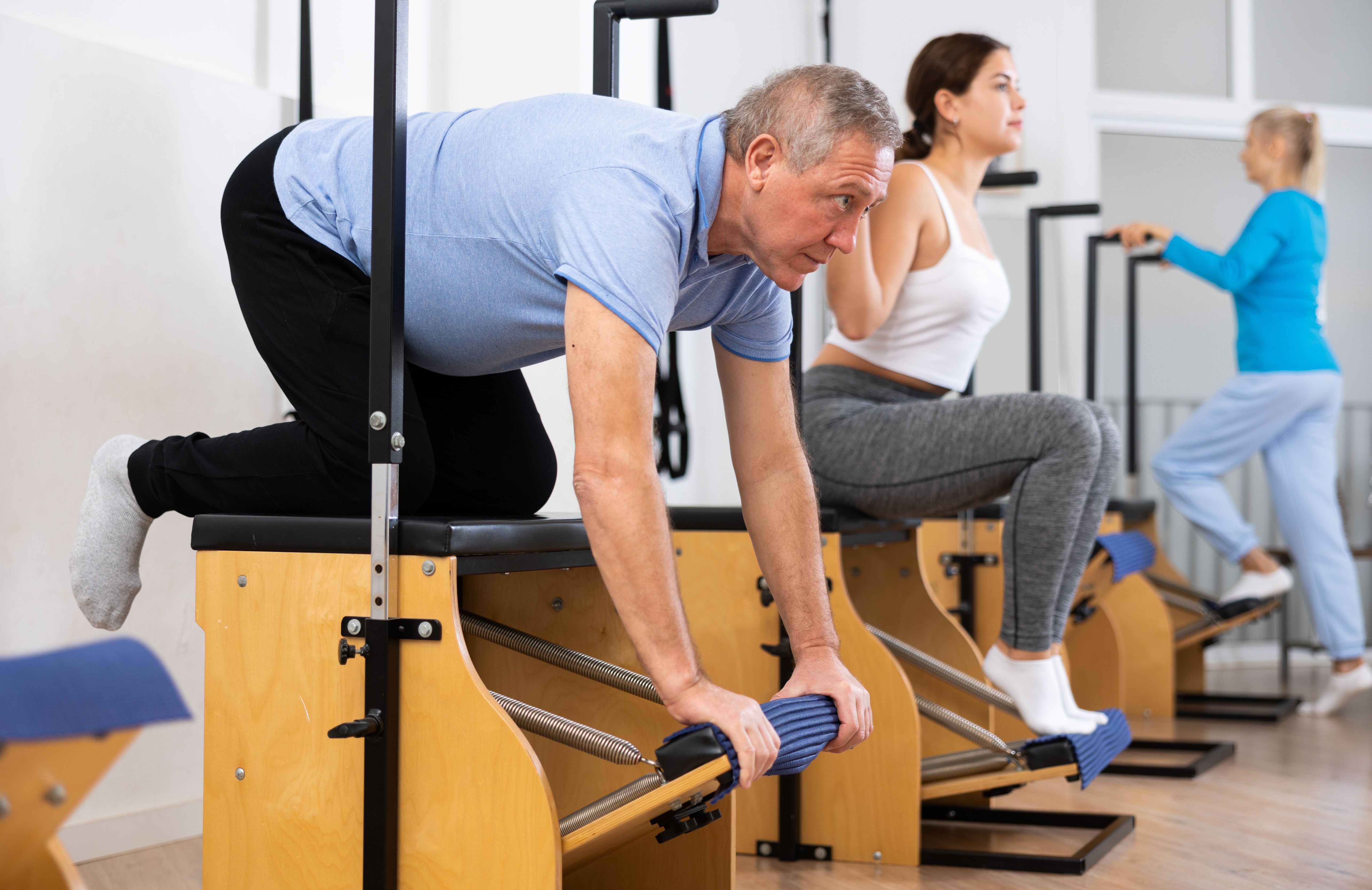 Senior male pensioner training hands and lower back while laying on Pilates Wanda chair in gym Senior male pensioner training hands and lower back while laying on Pilates Wanda chair in gym