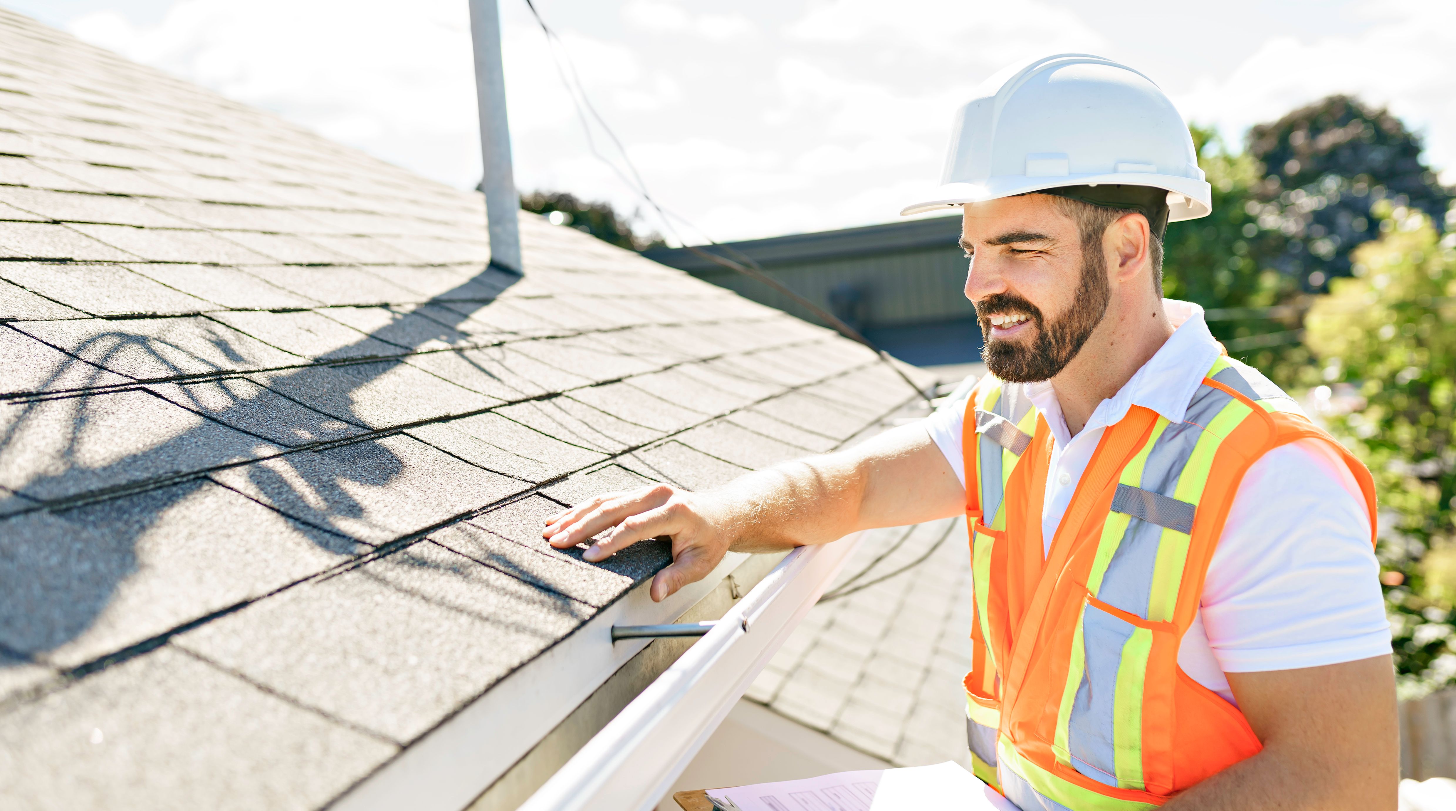 man in a hard hat, holding a clipboard, standing on the steps of an old rundown house.