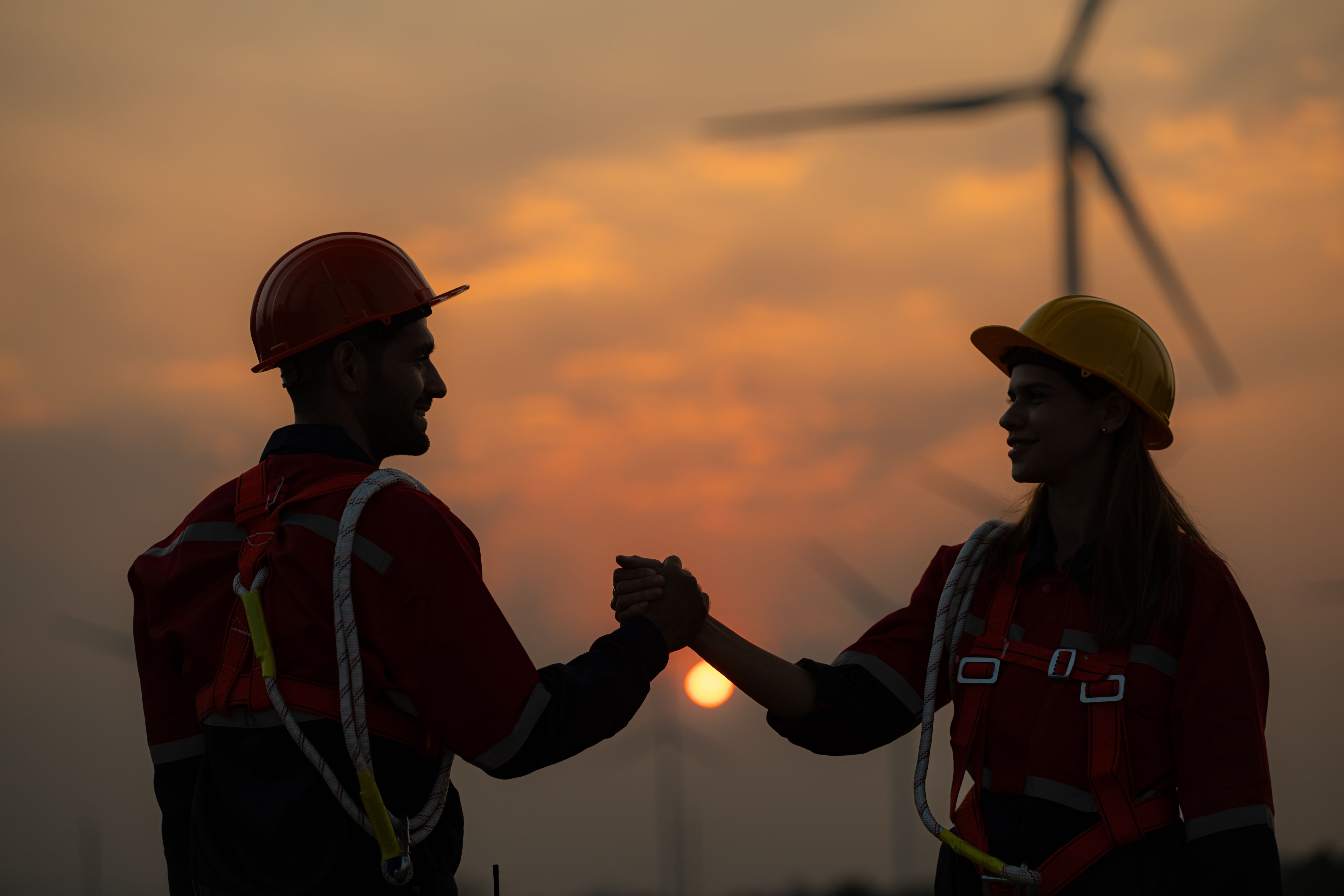 Engineers shake hands in a wind turbine farm with sunset background at the end of the day.