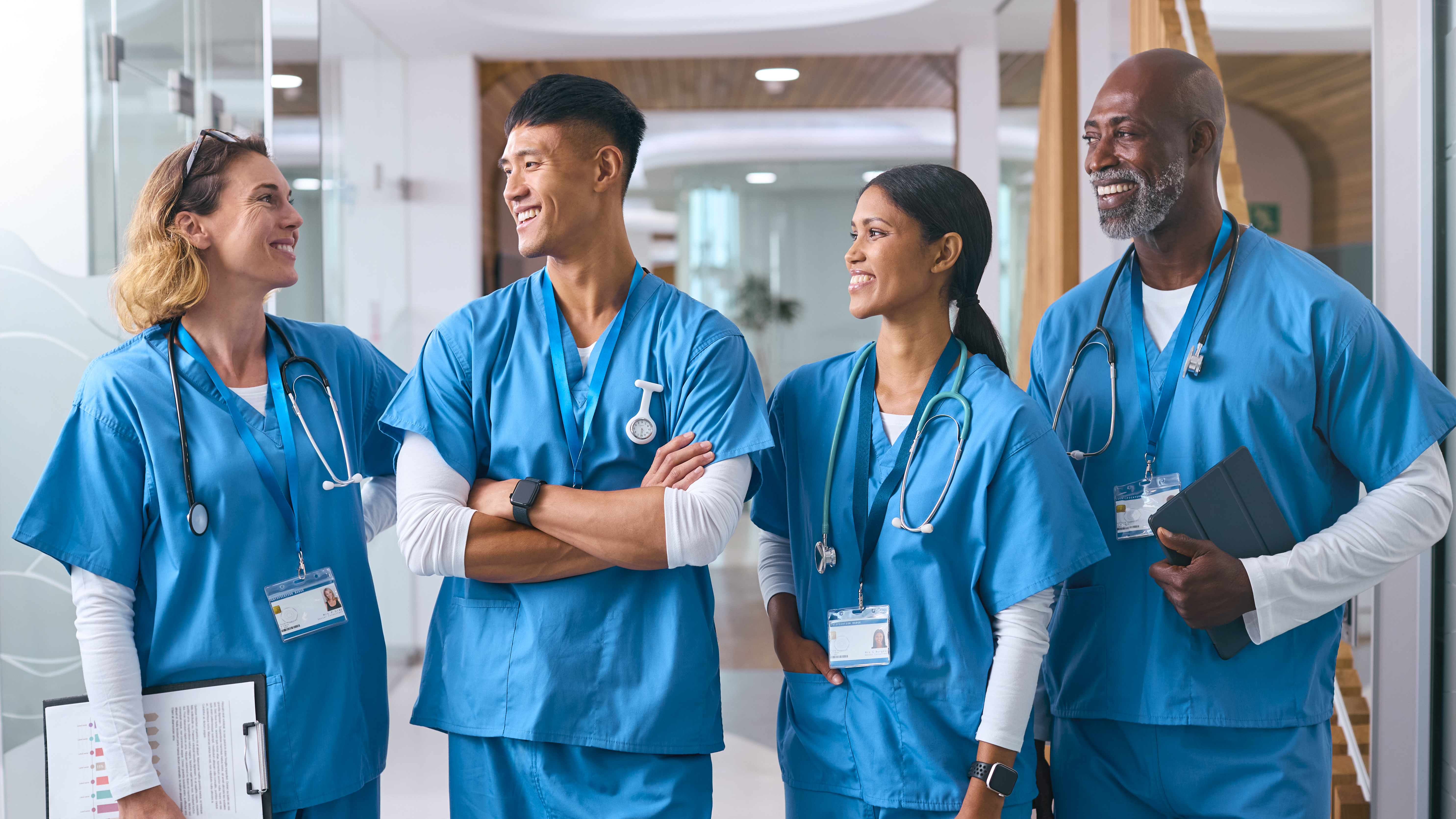 Smiling Multi Cultural Medical Team Wearing Scrubs Talking In Modern Hospital