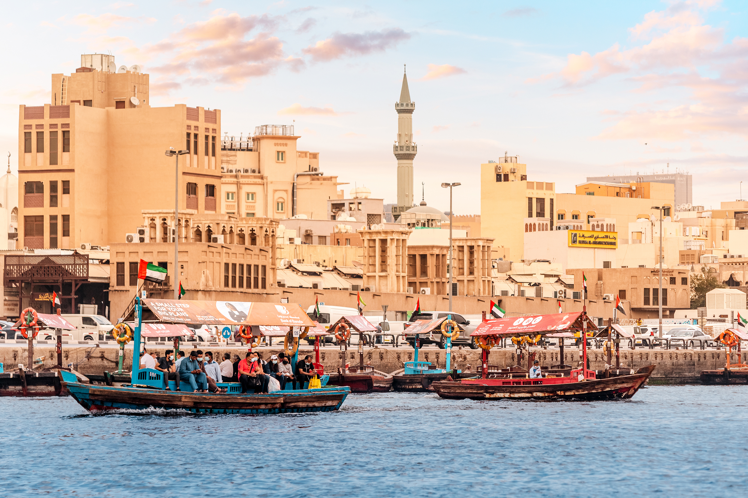 Abra Dhow wooden boats transport passengers from one bank of the Dubai Creek to the other with mosque minaret at the background