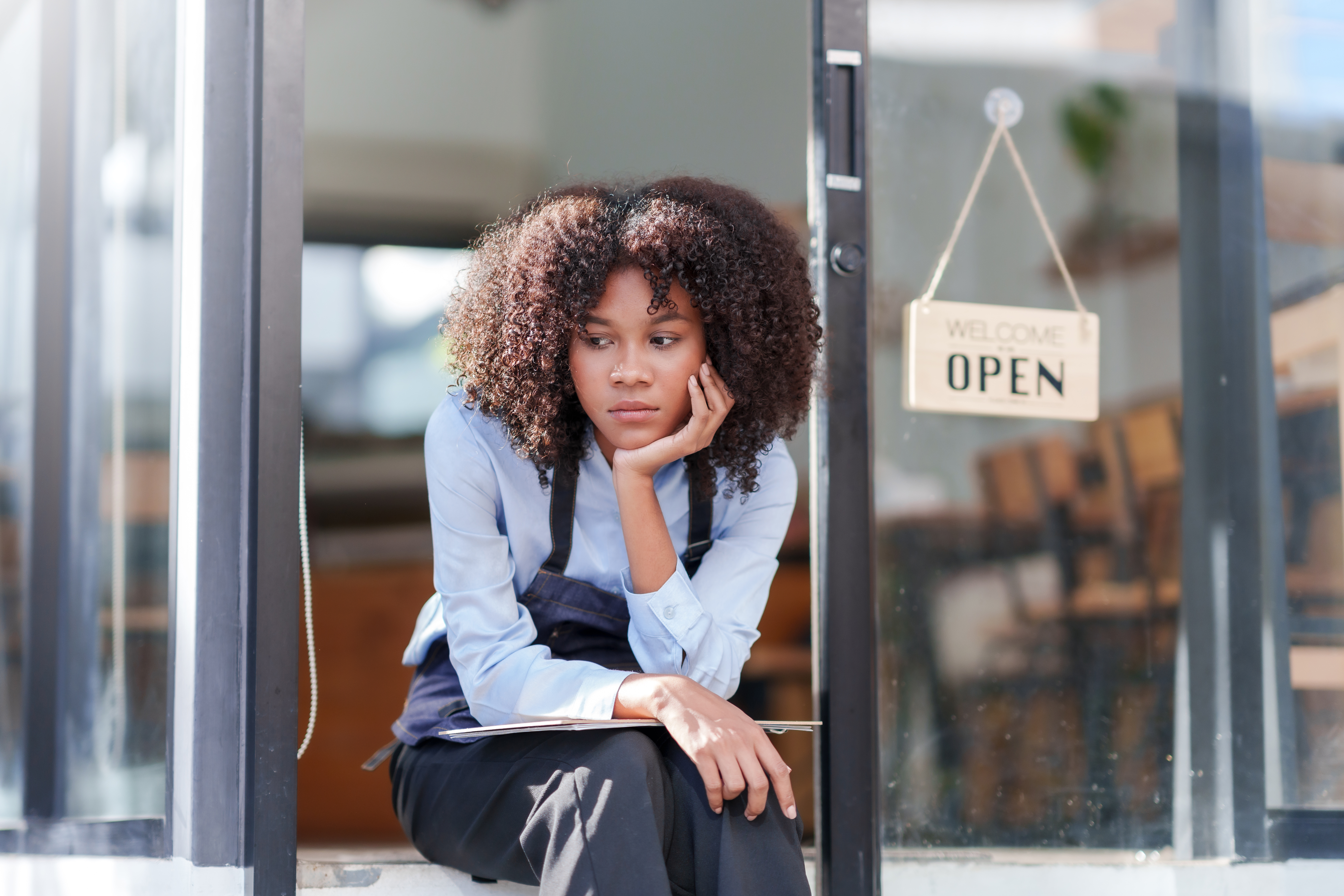 Female shopkeeper sitting stressed out at the store entrance frustrated by the economic impact. Female shopkeeper sitting stressed out at the store entrance frustrated by the economic impact.