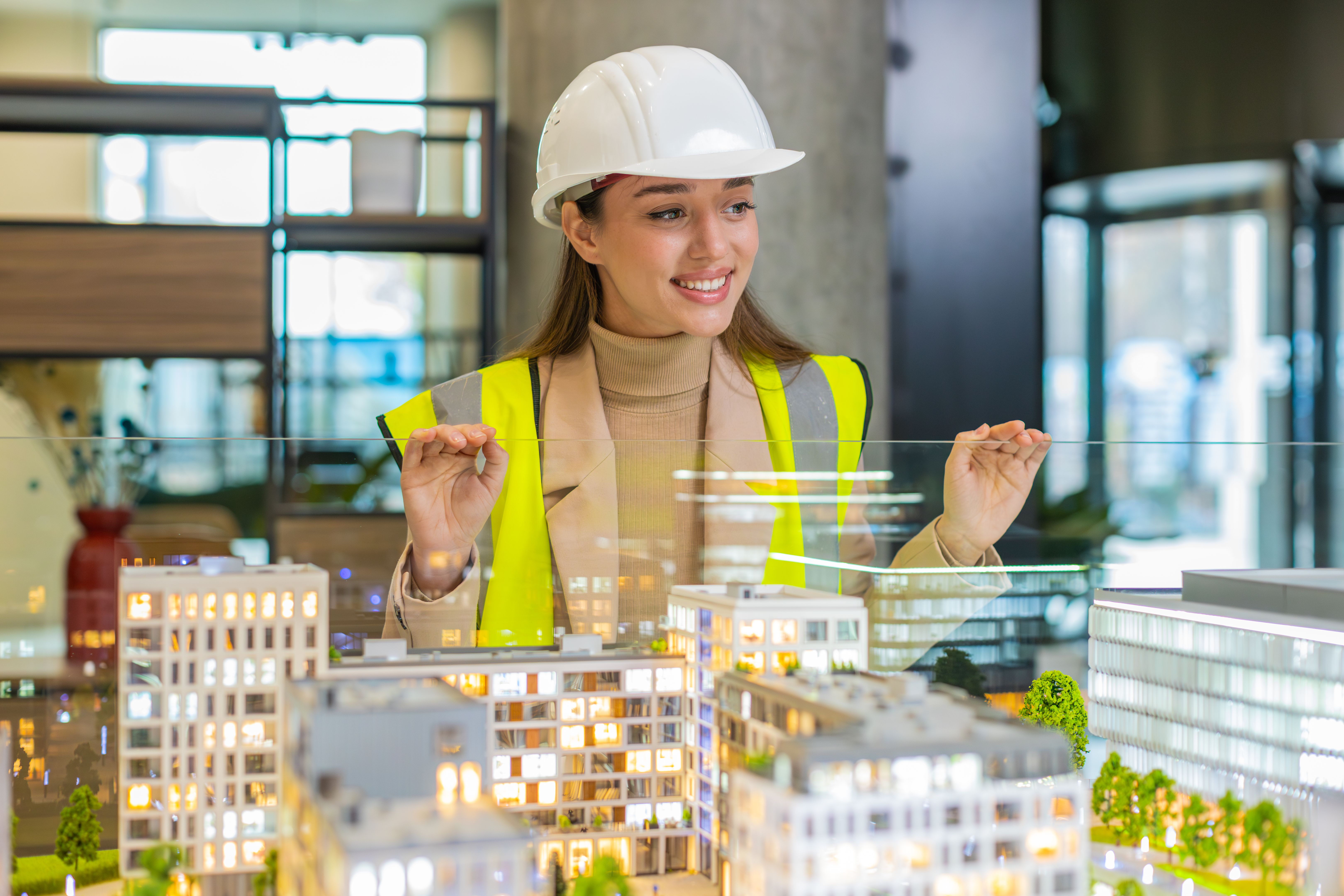 Confident young female architect in hardhat analyzing office complex architectural model in office