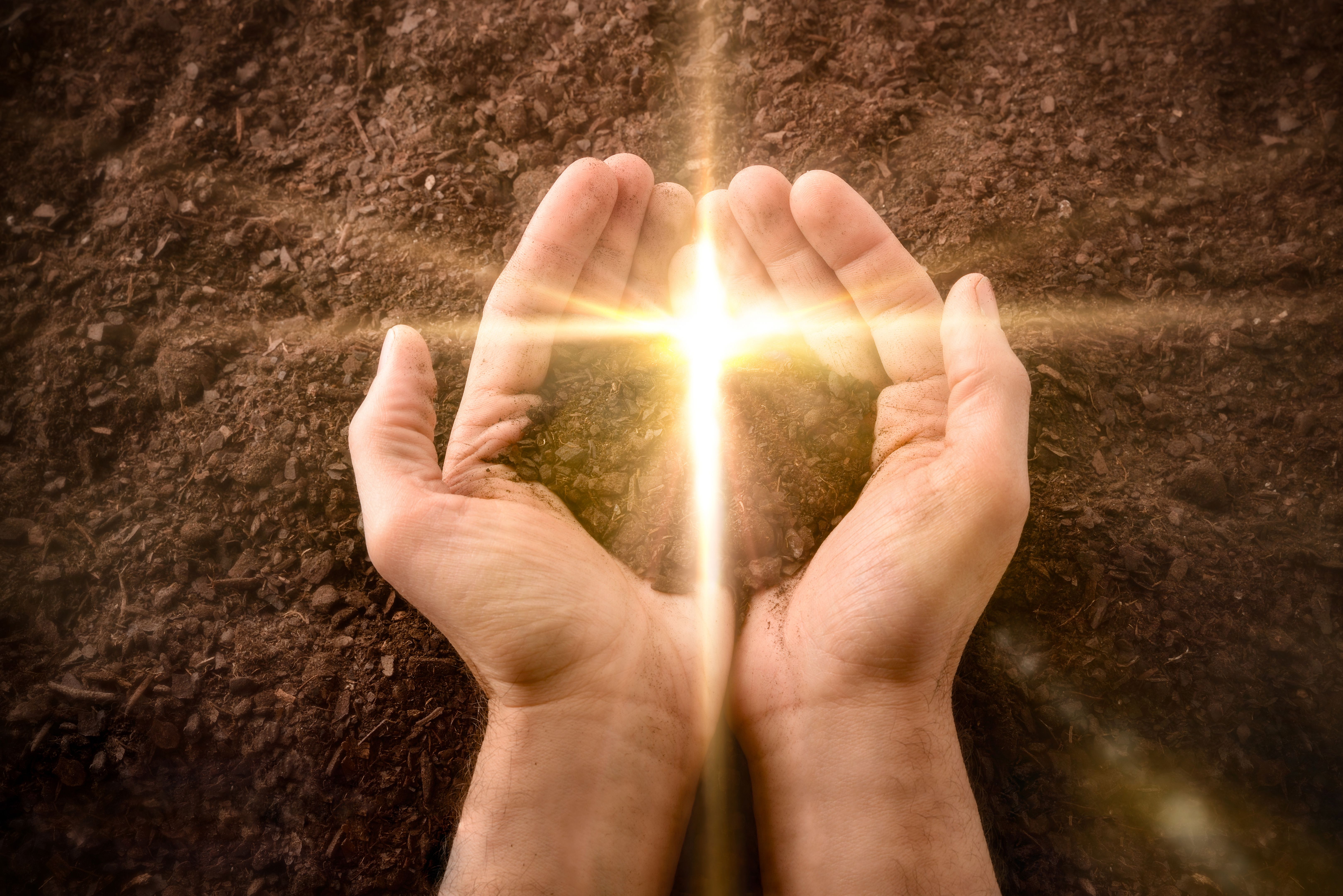 Hands with a pile of dirt with a cross-shaped flash