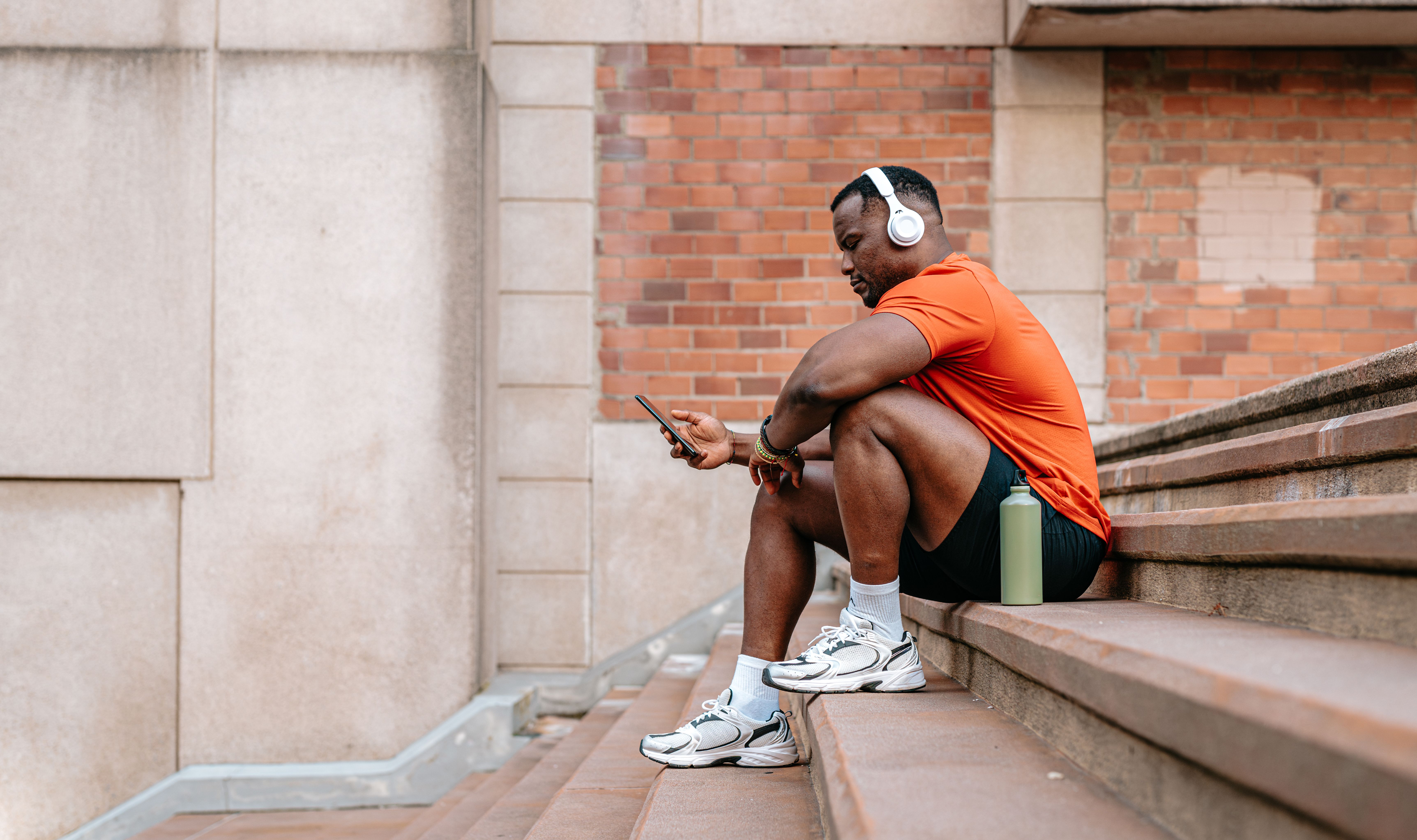 Afro american athlete sitting on stairs and using smartphone after training