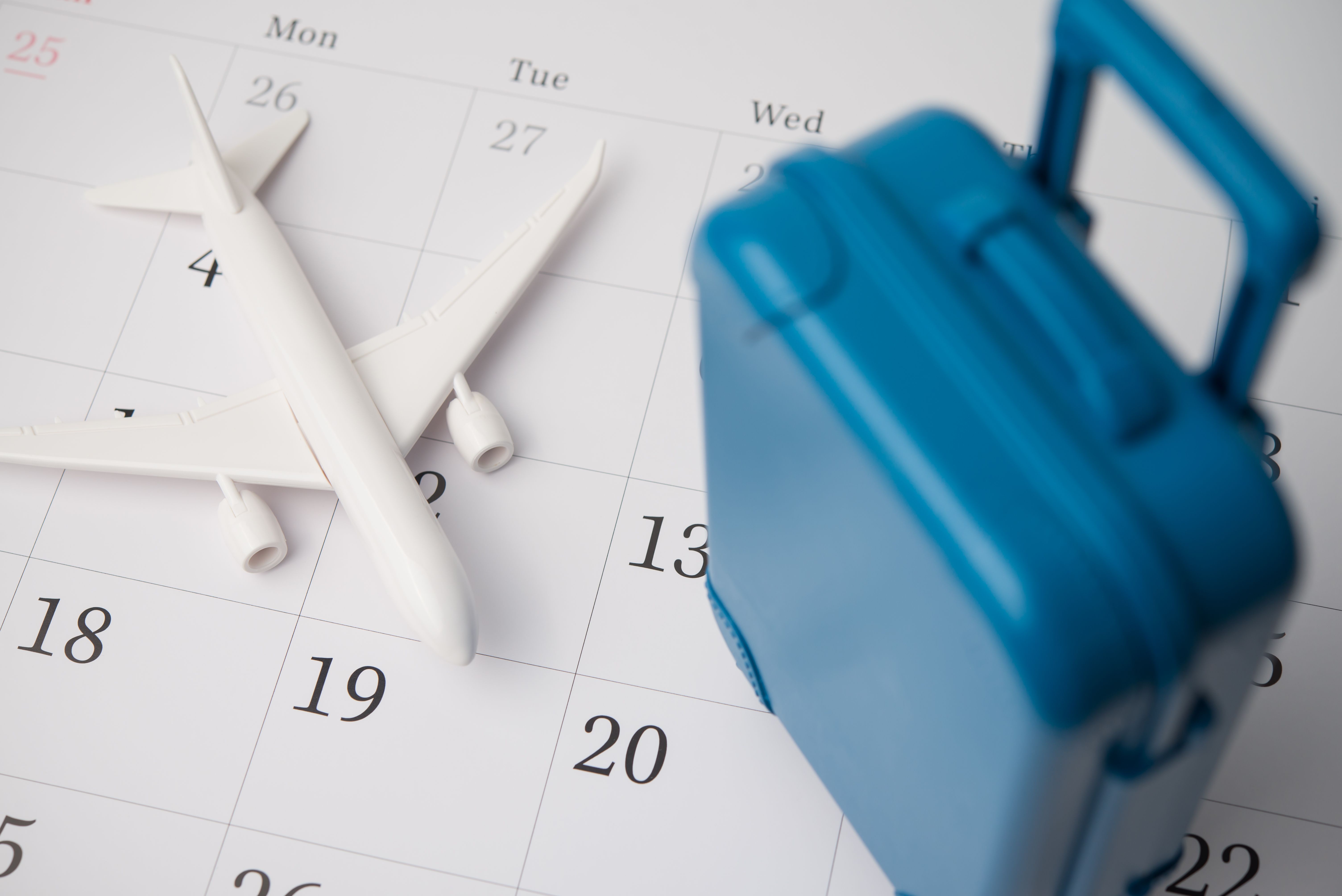 Travel suitcase and airplane on blank white calendar background.