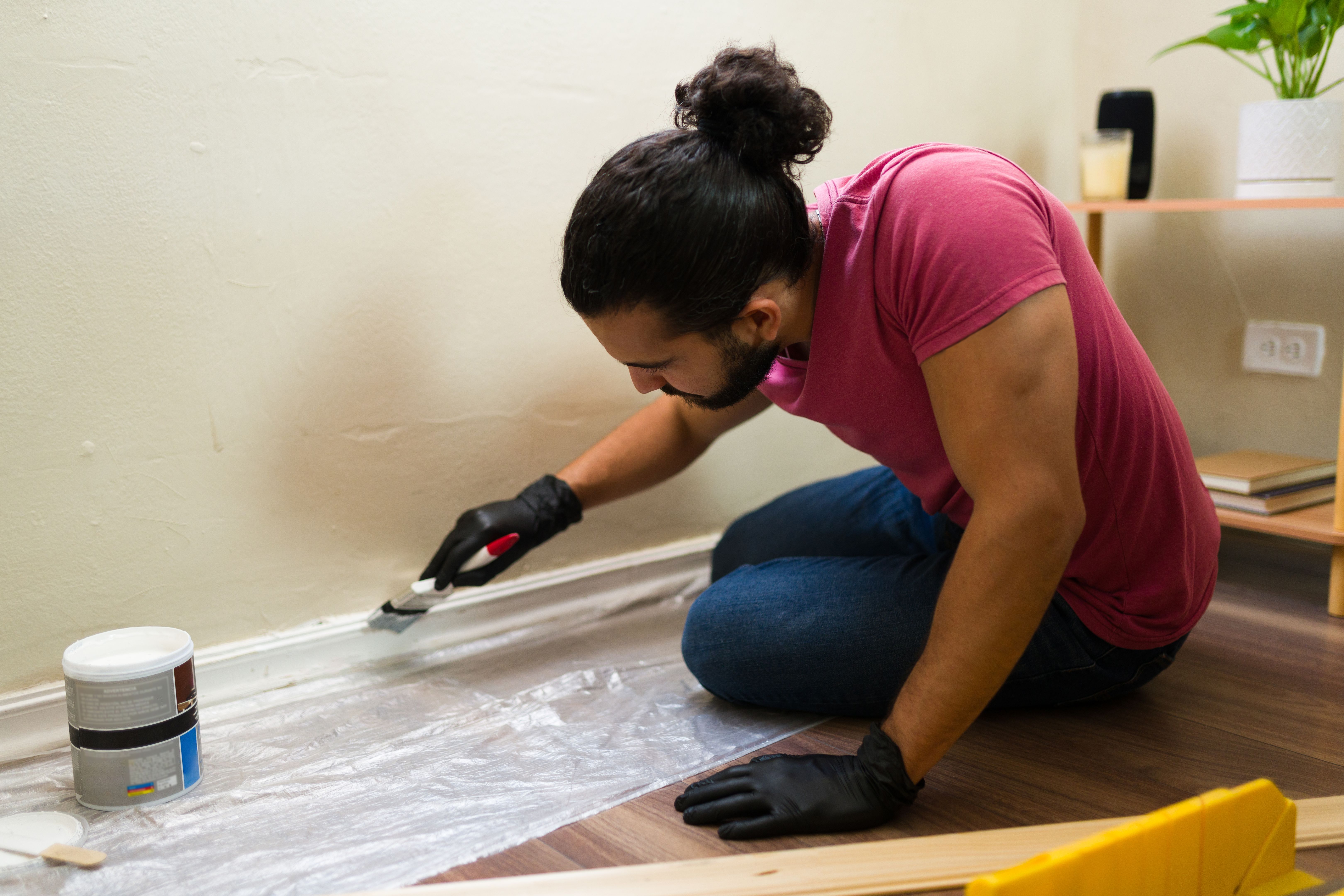 Man painting skirting board in modern apartment while renovating home
