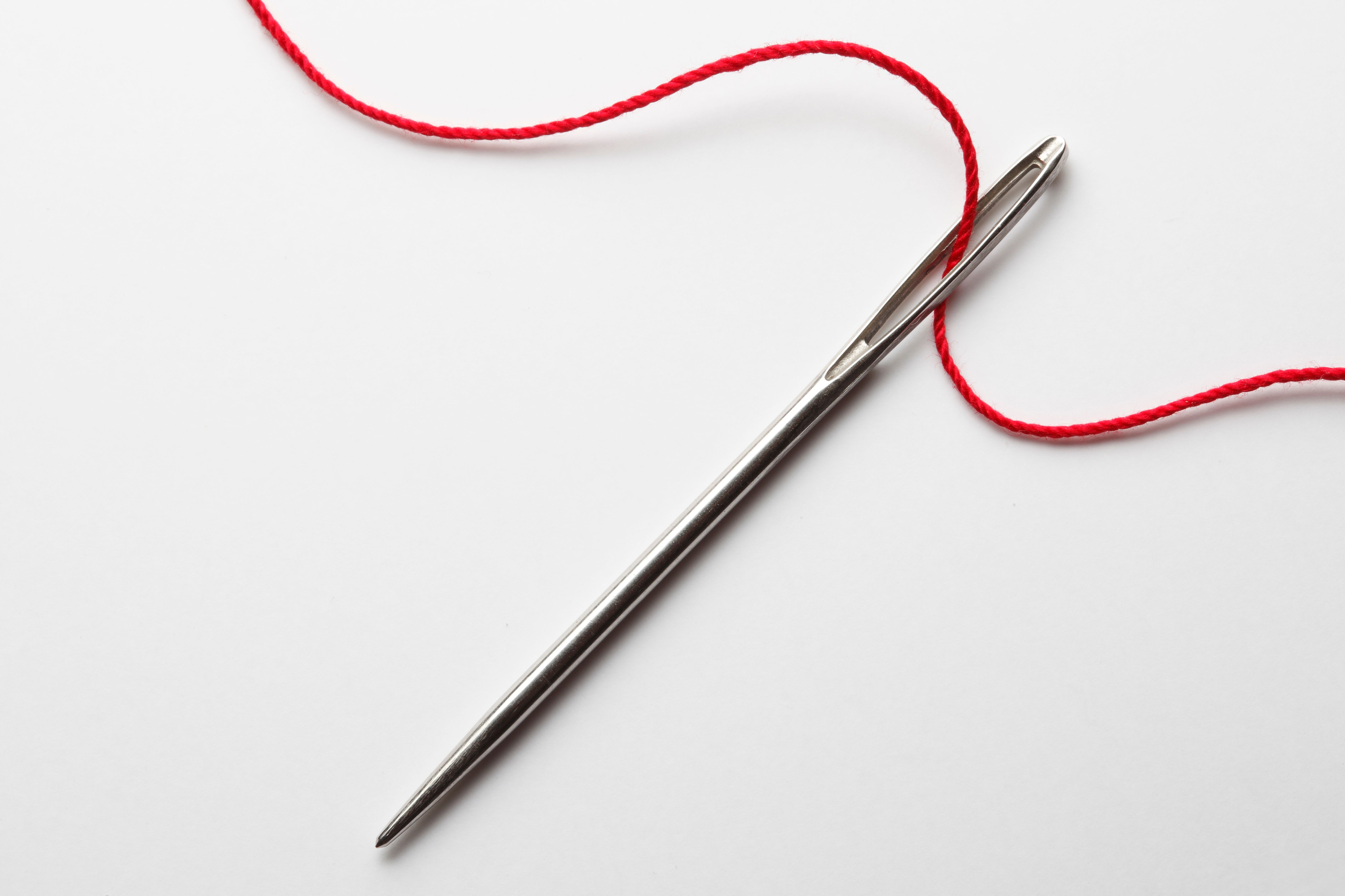 Close up of threading eye of a needle with red thread