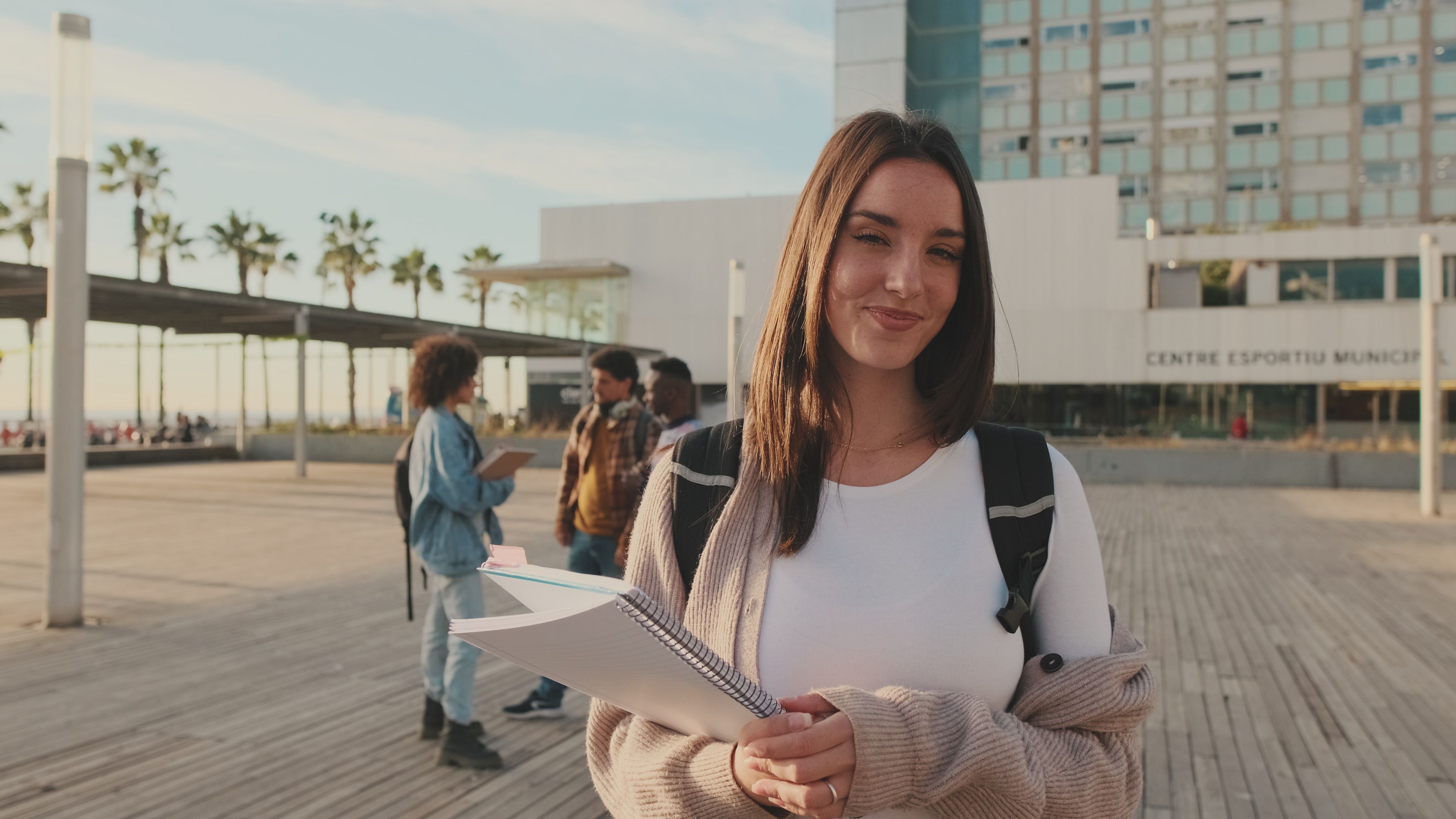 Girl is smiling while looking at the camera. Student with notebooks in her hands looks at the camera and smiles