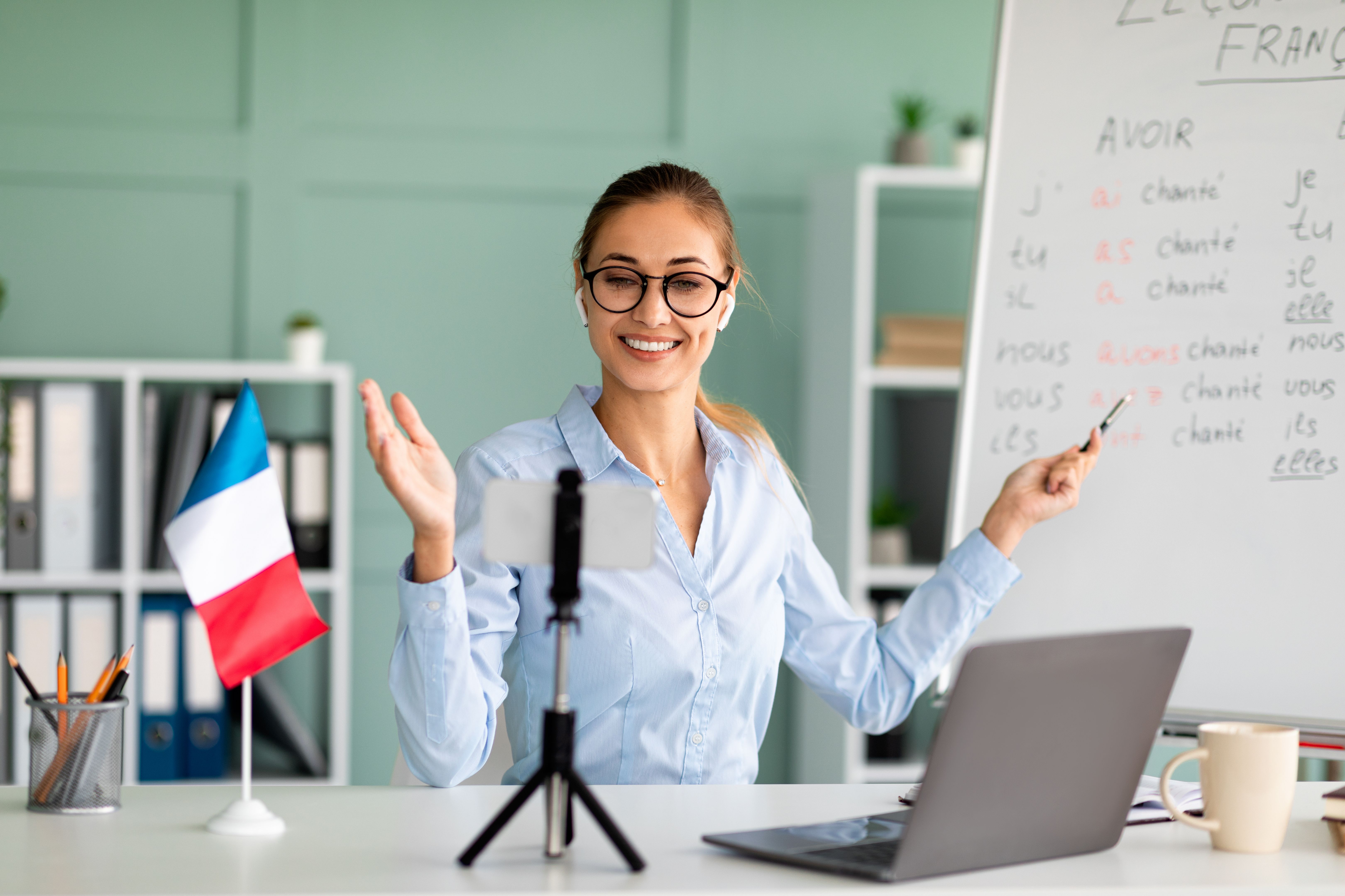 Tuteur de langues étrangères positif enseignant Français en ligne à l’aide d’un smartphone et d’un ordinateur portable, donnant des conférences à distance