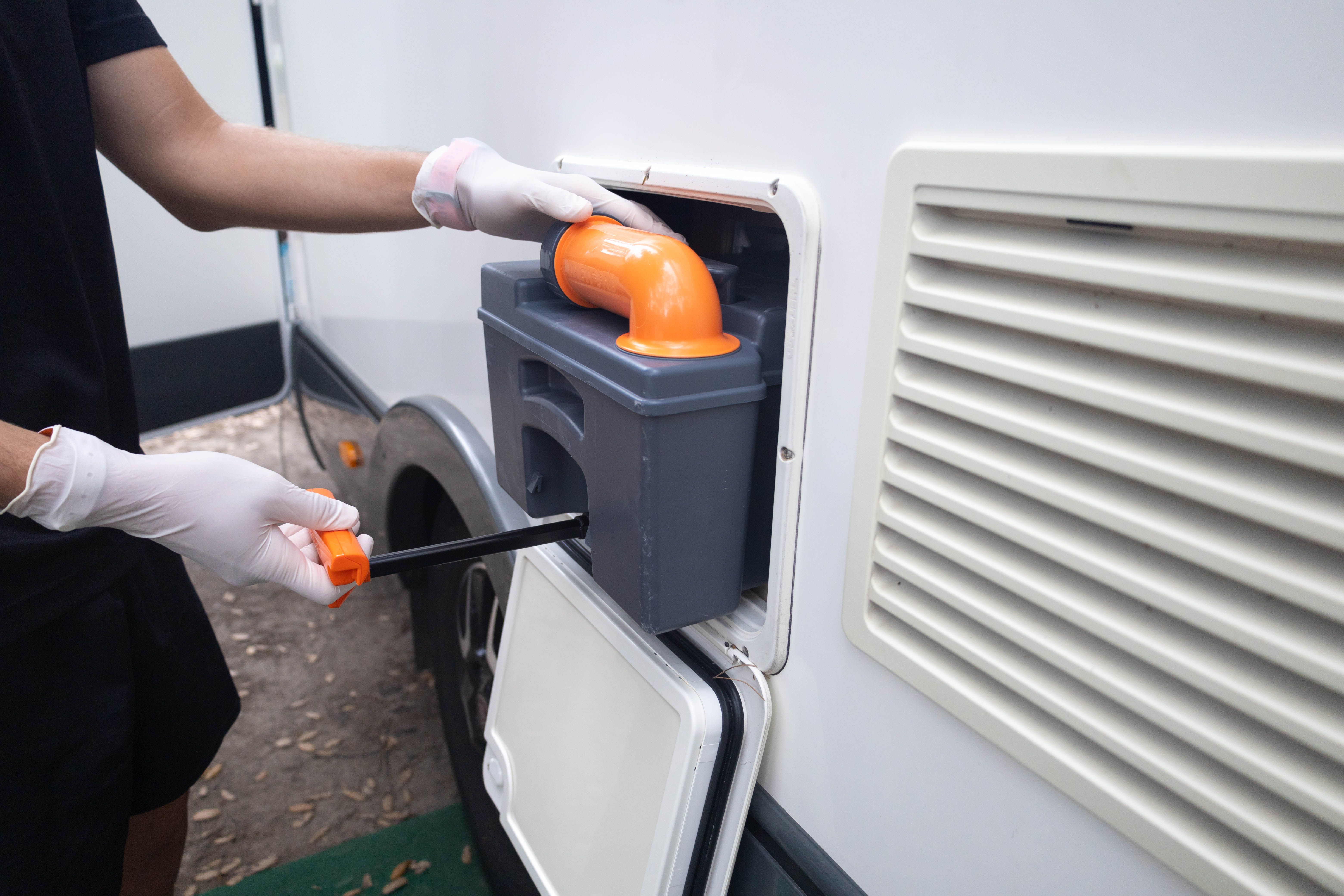Man with gloves making the mobile home maintenance, taking out the raw sewage from the toilet to empty it.