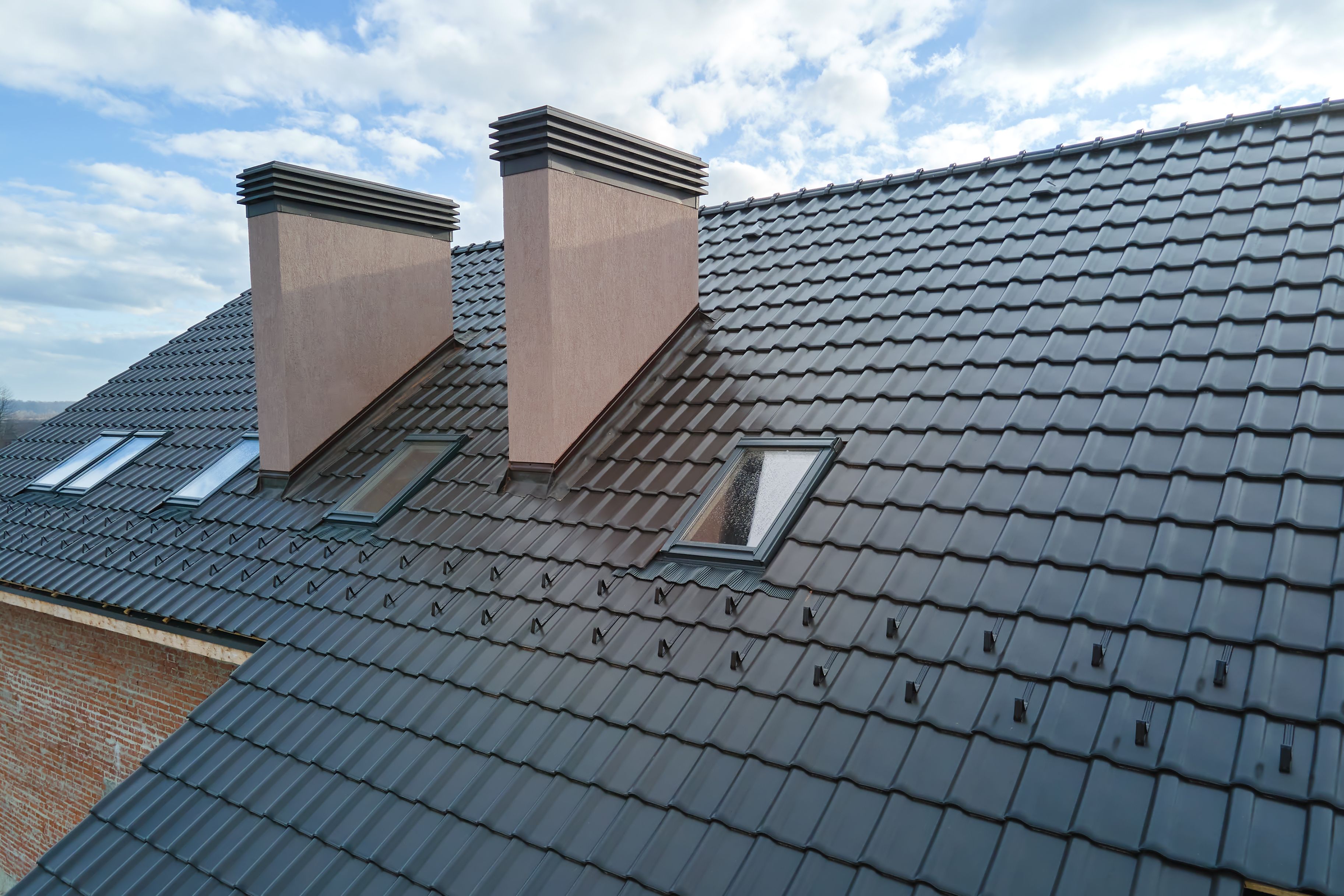 Closeup of attic windows and brick chimneys on house roof top covered with ceramic shingles. Tiled covering of building