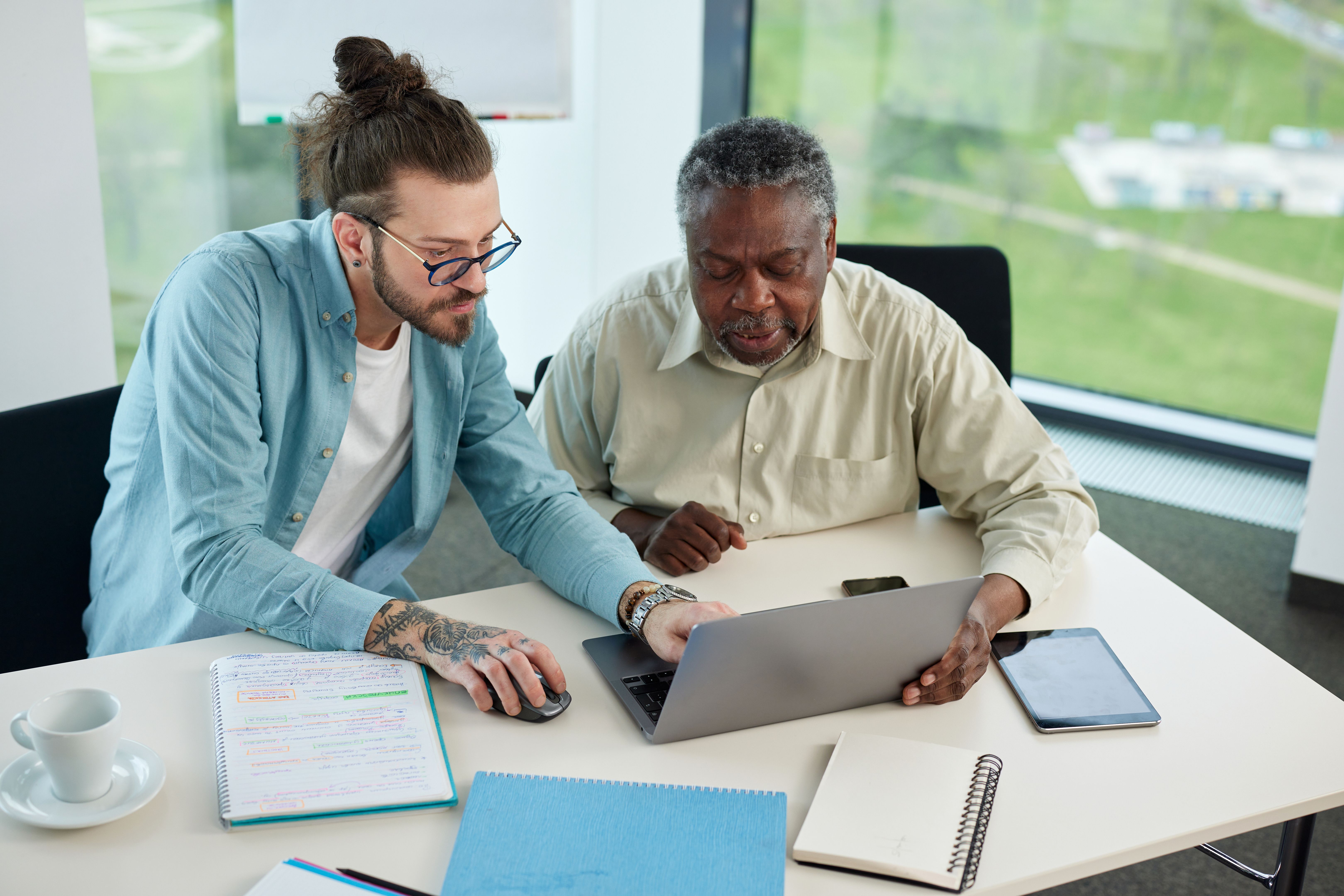 A young teacher explaining to senior student how do computer programming on a laptop.