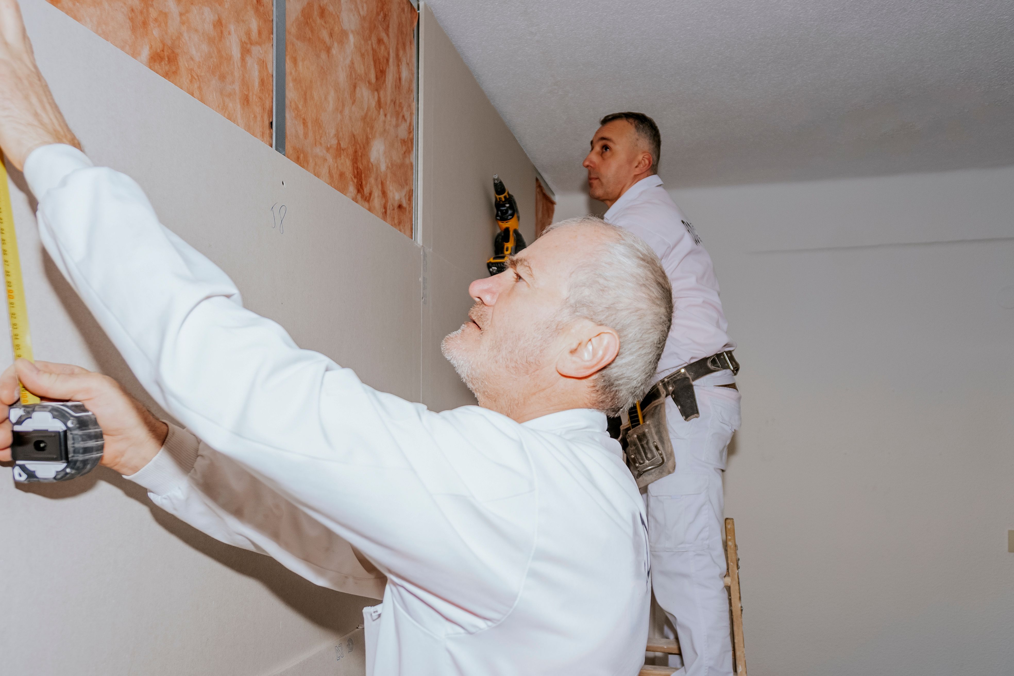Two workers installing plasterboard panels with acoustic insulation.