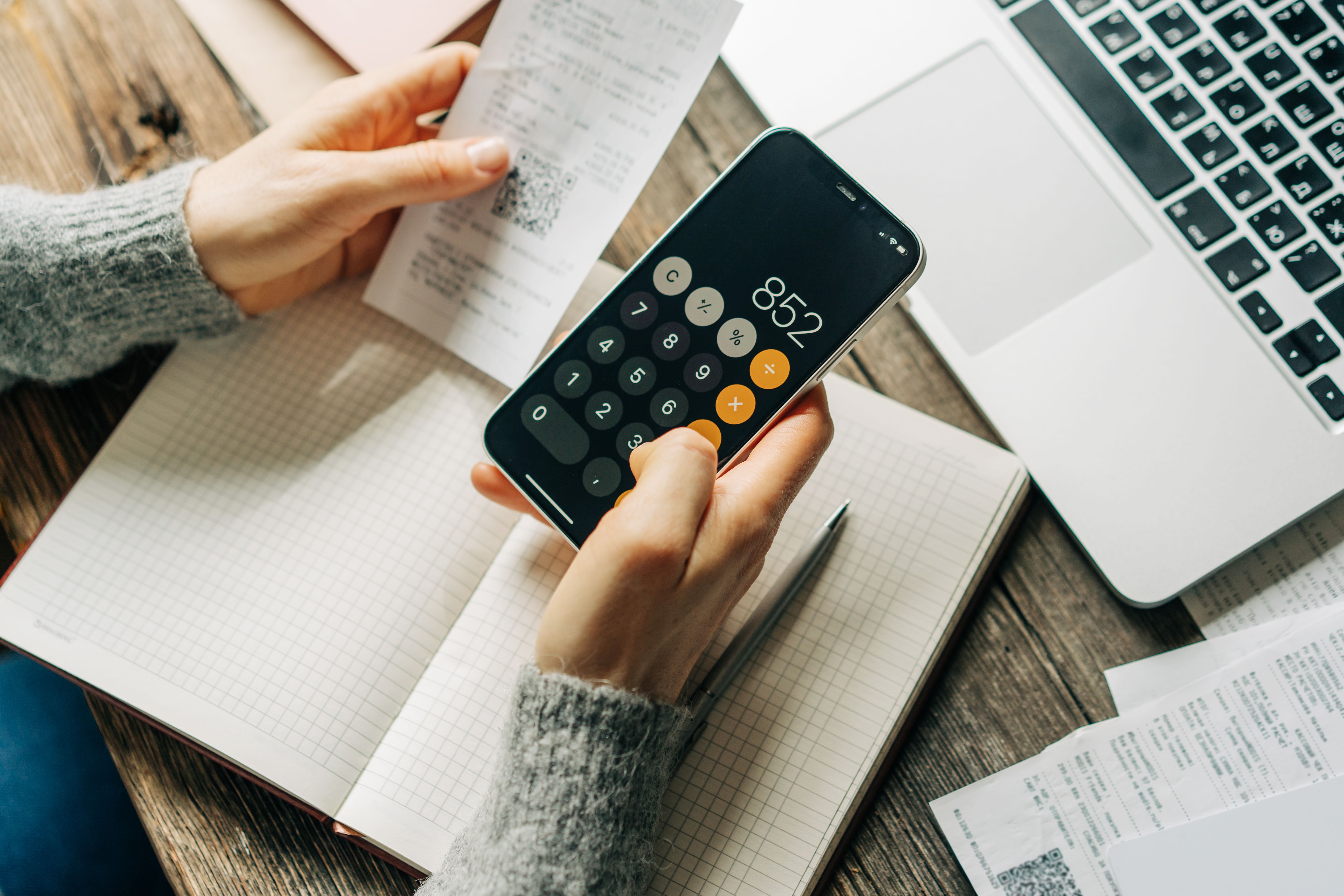 Unrecognizable woman works at her desk with bills using a calculator on her mobile phone.