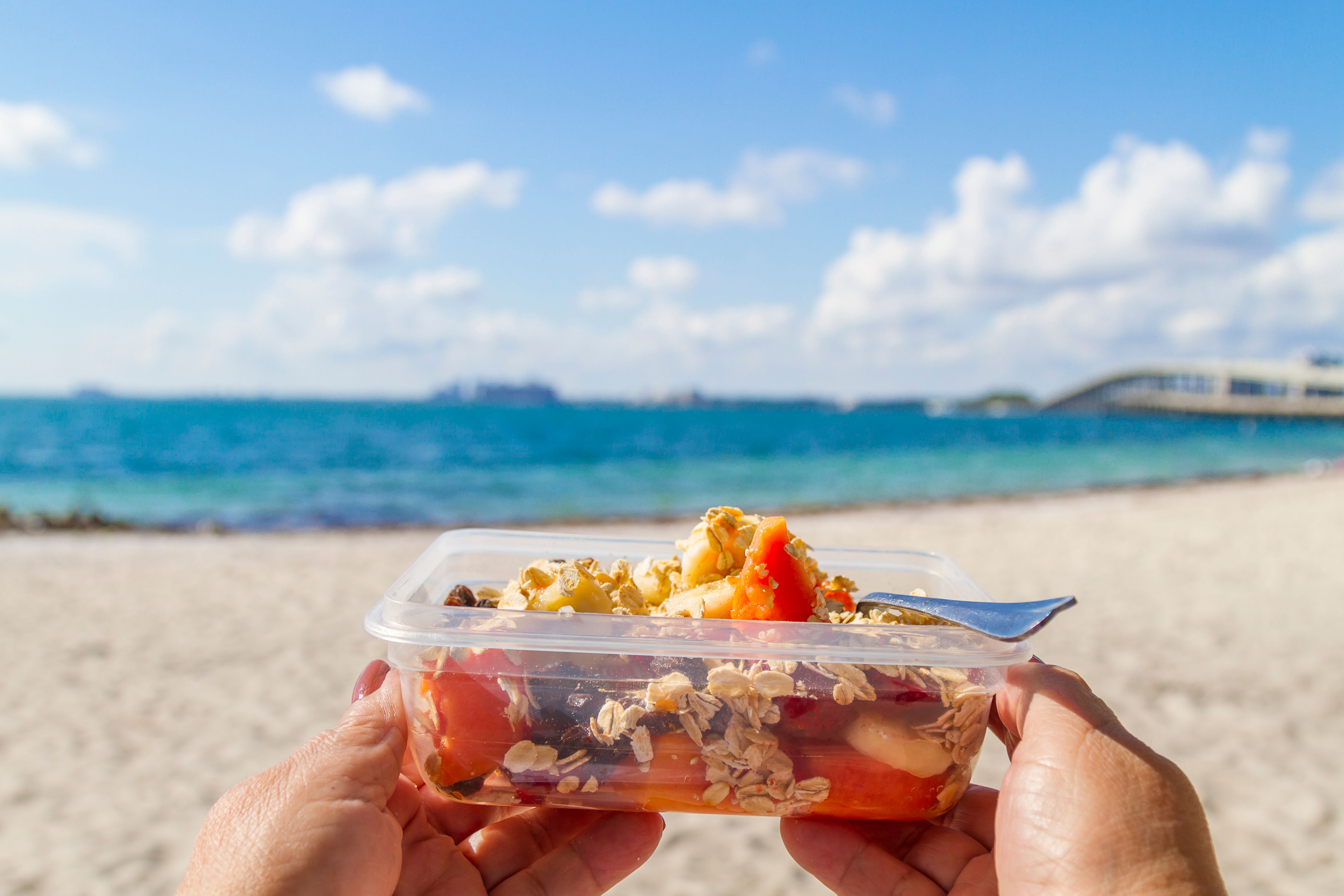 someone at the beach holding a plastic container with fruits and granola