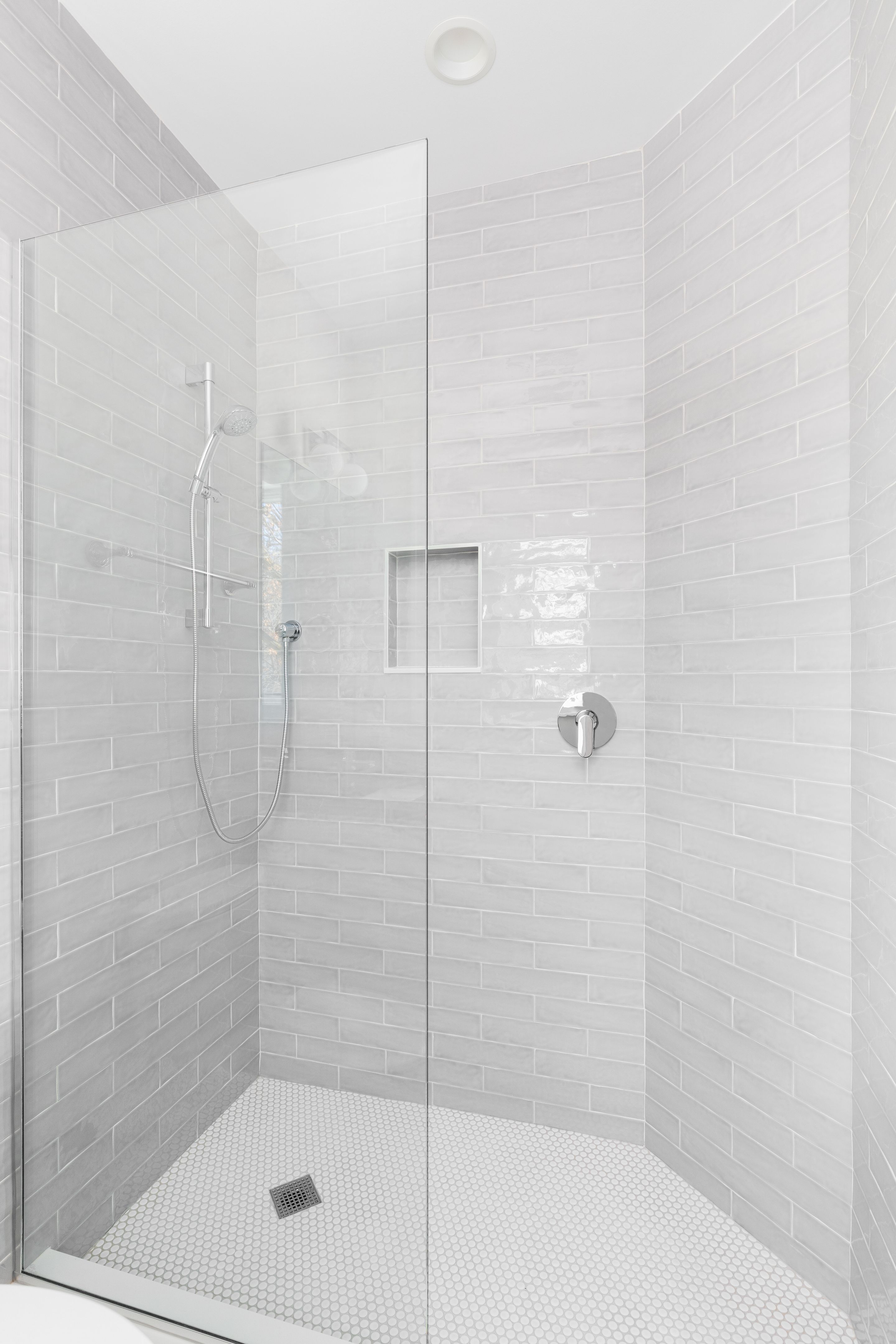 A walk-in shower with grey subway and white circular tiles.