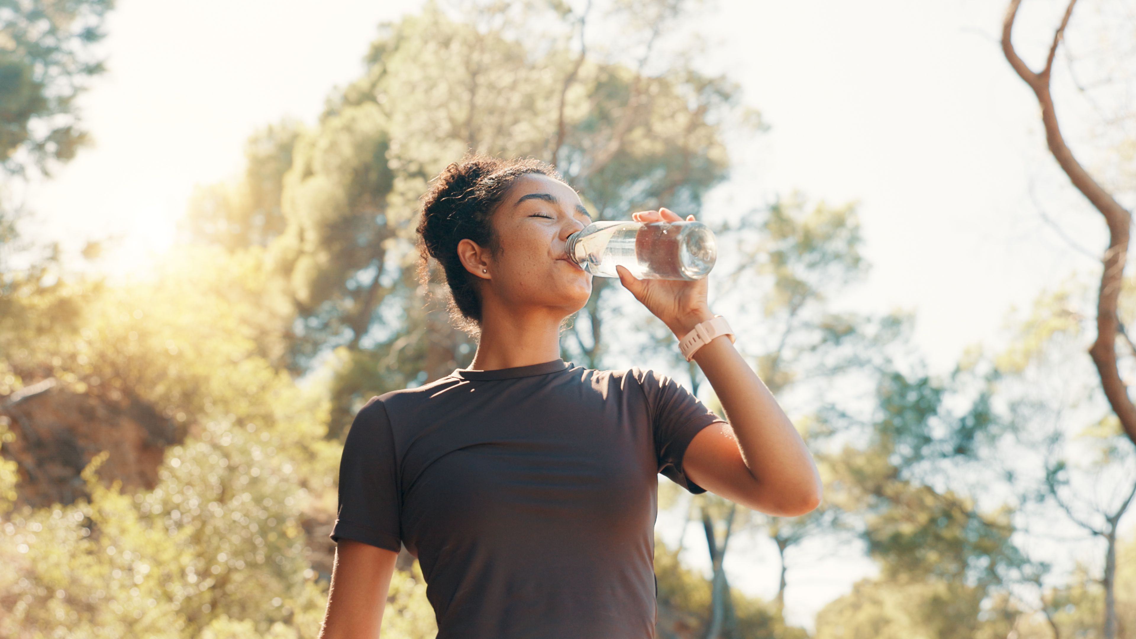 Woman, drinking water and thirsty in nature for fitness, electrolytes and body detox. Low angle, runner and bottle with H2O for hydration, exercise break and liquid for gut health or digestion aid