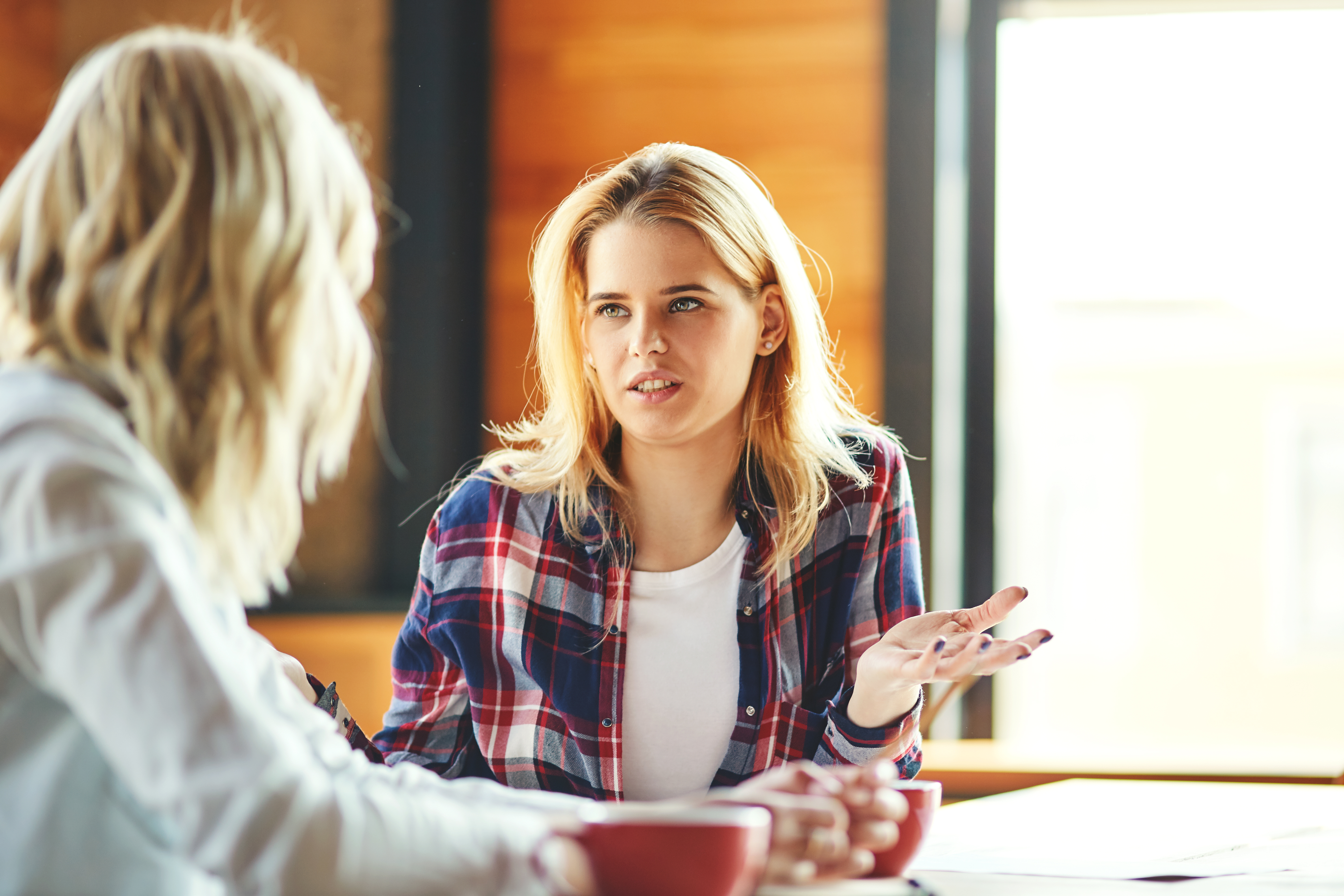 Two young female friends chatting over coffee in cafe. Blonde women discussing issues Two young female friends chatting over coffee in cafe. Blonde women discussing issues