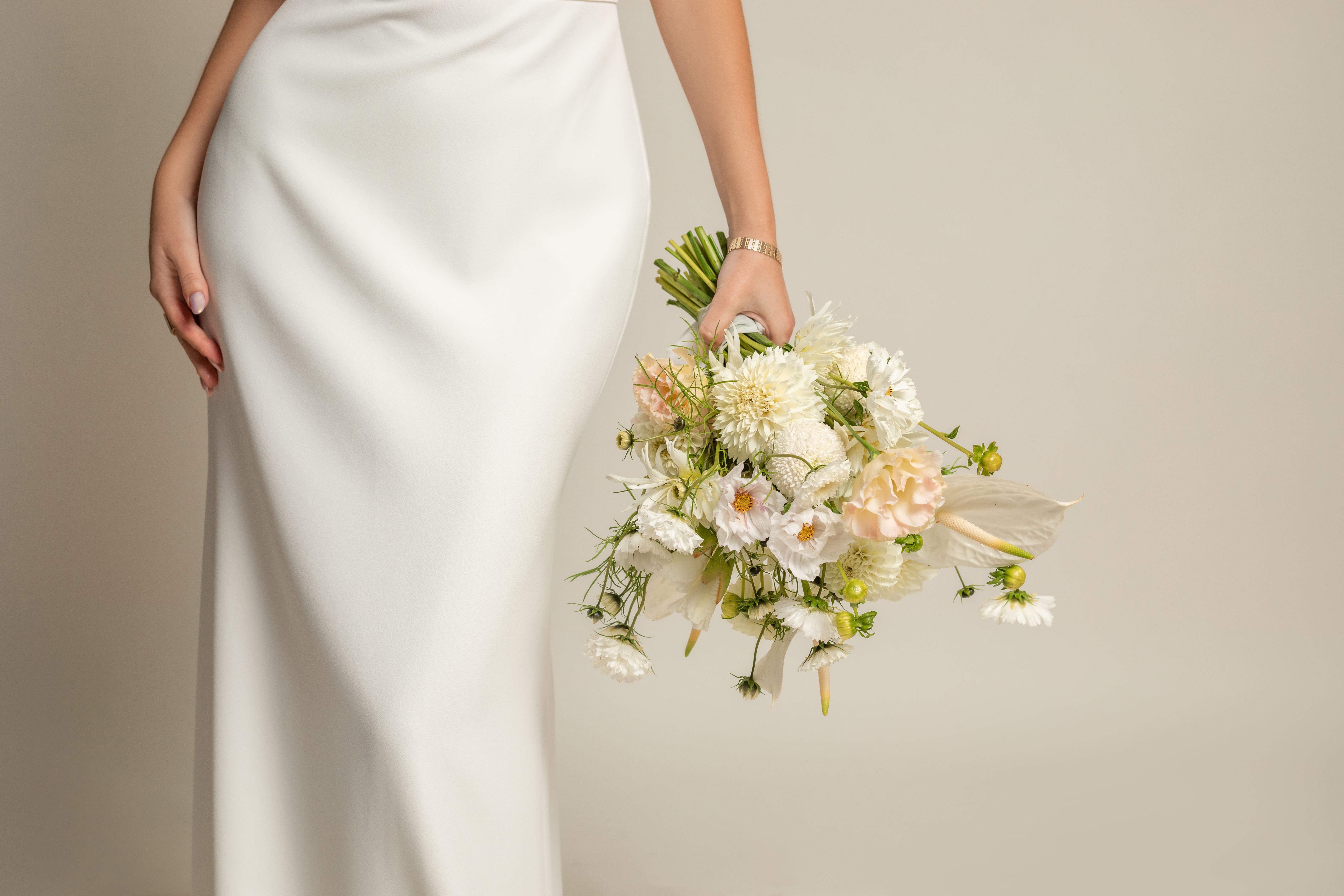 Femme recadrée méconnaissable en élégante robe de soie blanche avec bouquet blanc de fleurs naturelles à la main avec accessoires Femme recadrée méconnaissable en élégante robe de soie blanche avec bouquet blanc de fleurs naturelles à la main avec accessoires