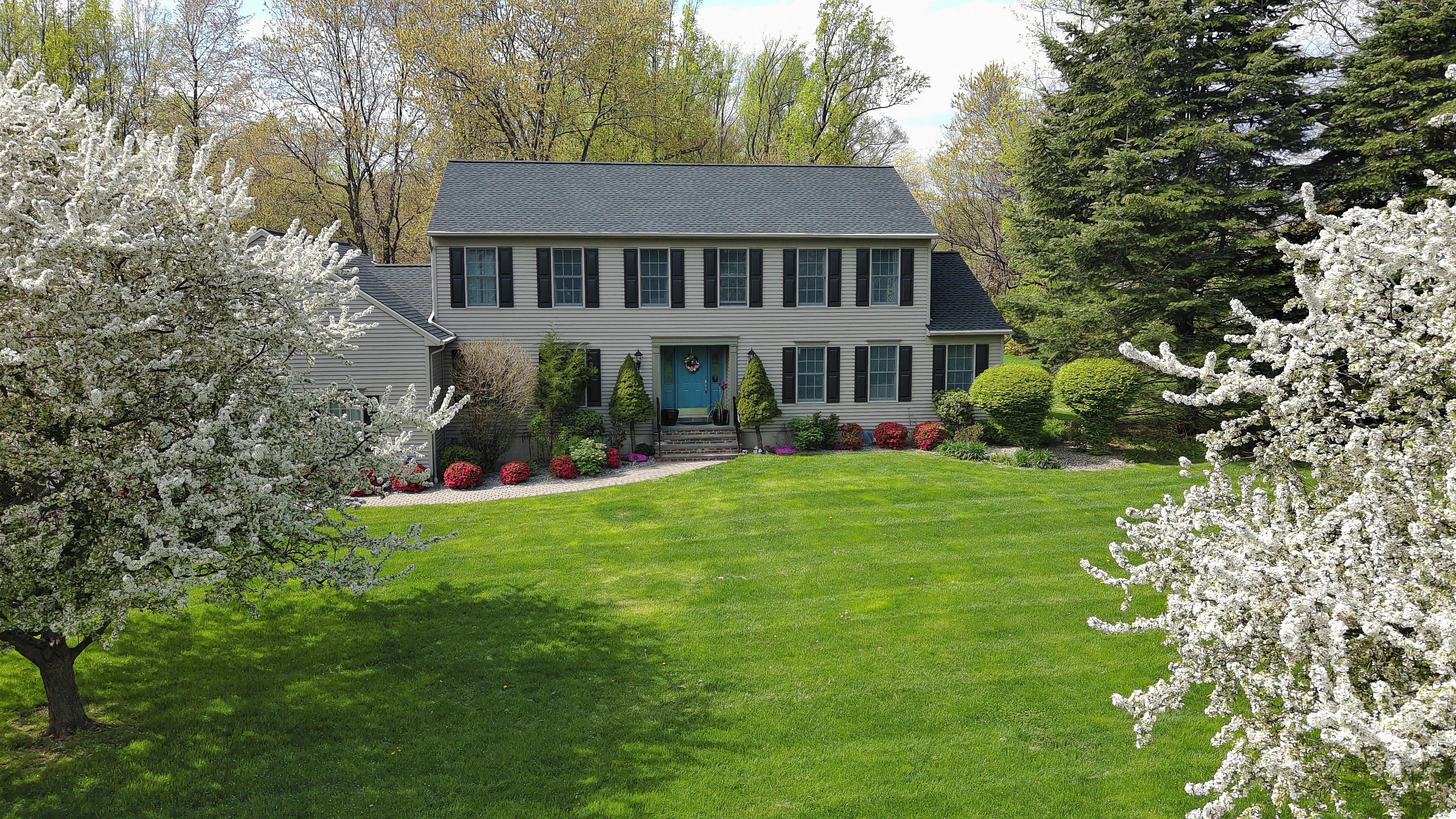 Two story residential house is surrounded by lush greenery and blooming apple trees in New Jersey