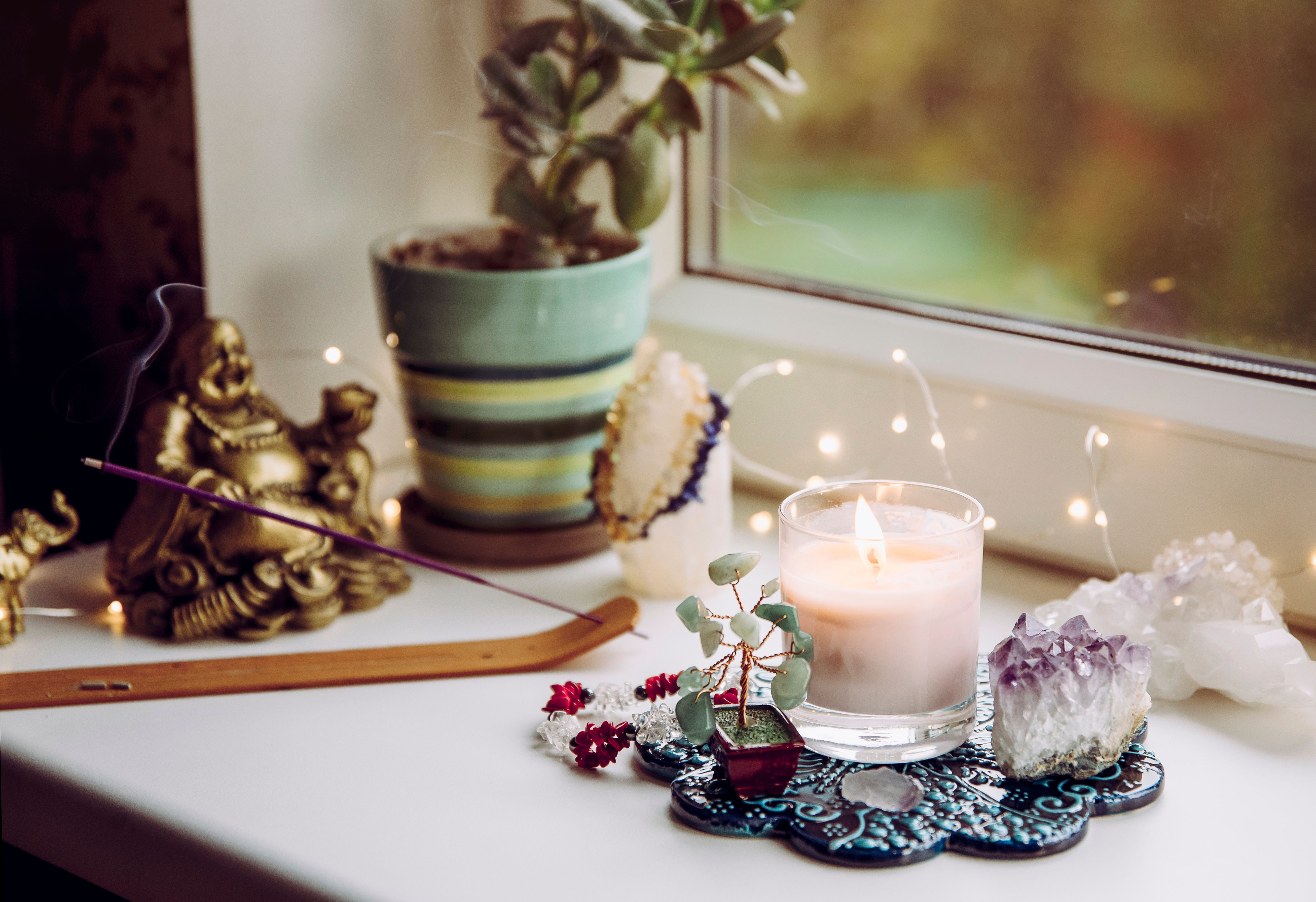 Feng Shui altar at home in living room or bed room. Attracting wealth and prosperity concept. Crystal clusters, wire tree with gemstones, golden smiling Buddha figure on table window sill.