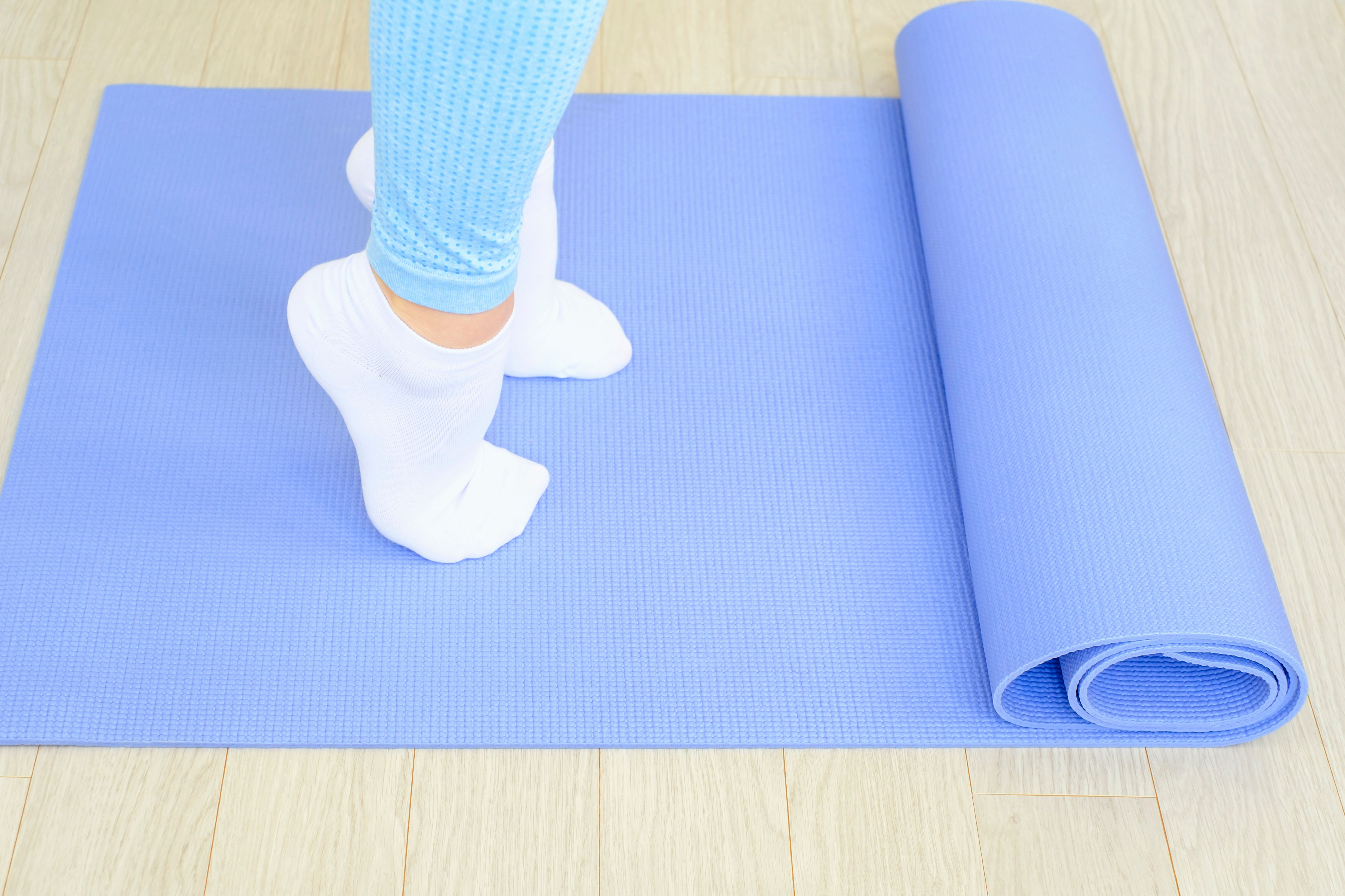 Female legs doing exercises lifting on toes close-up on blue background.