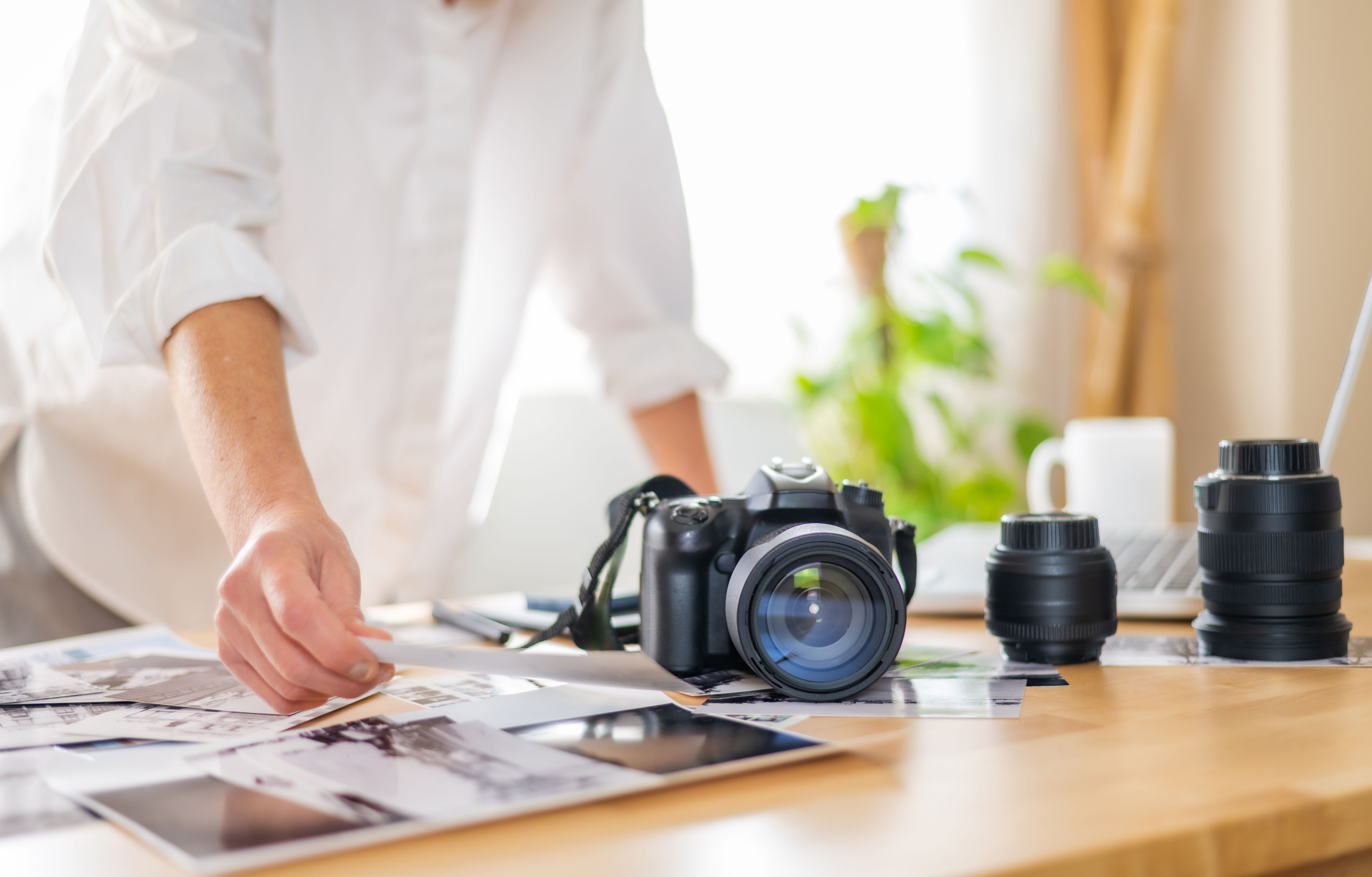 Female photographer selecting printed photos on a desk at her home office, with camera and lenses