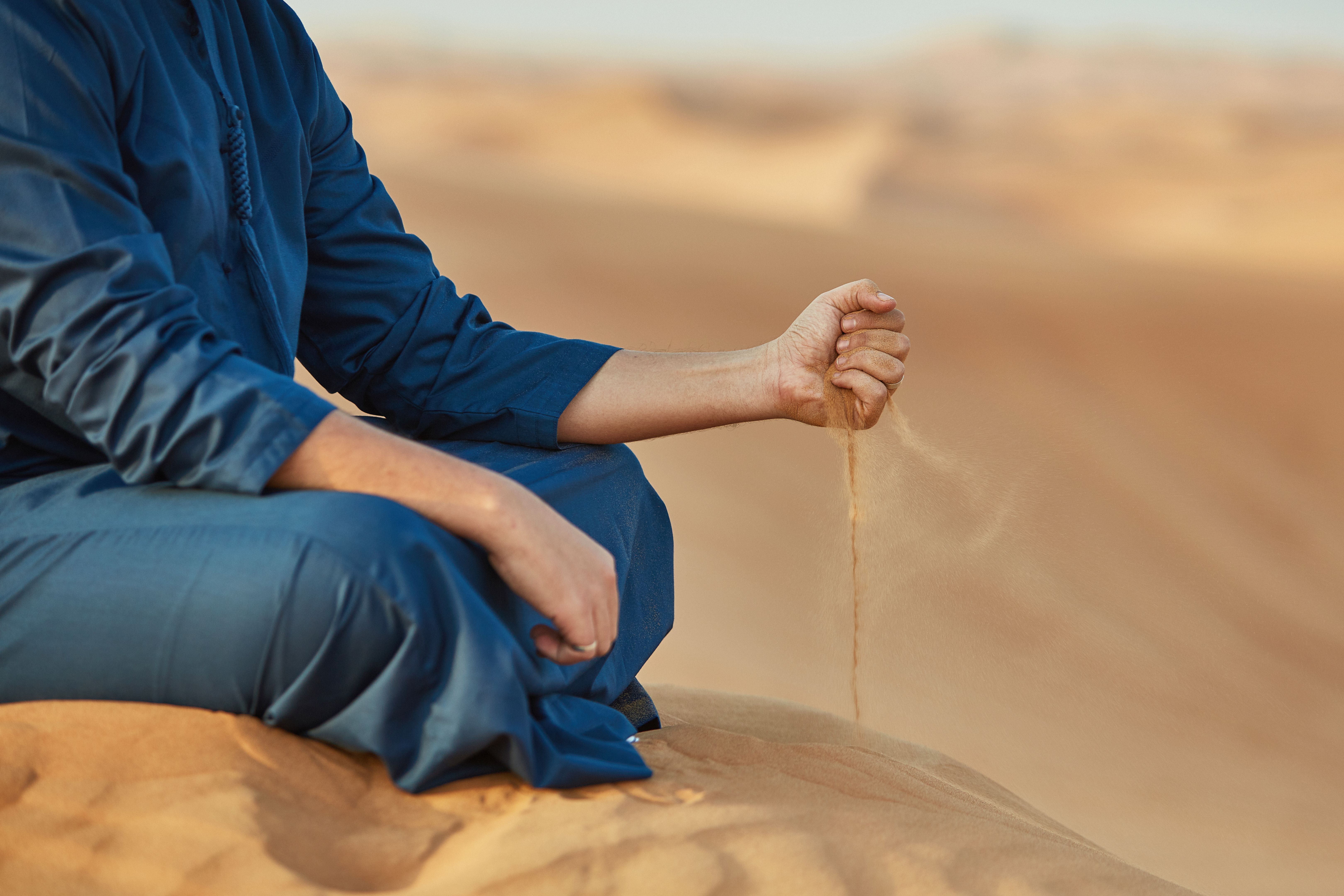 Low section of Arab man throwing sand in desert
