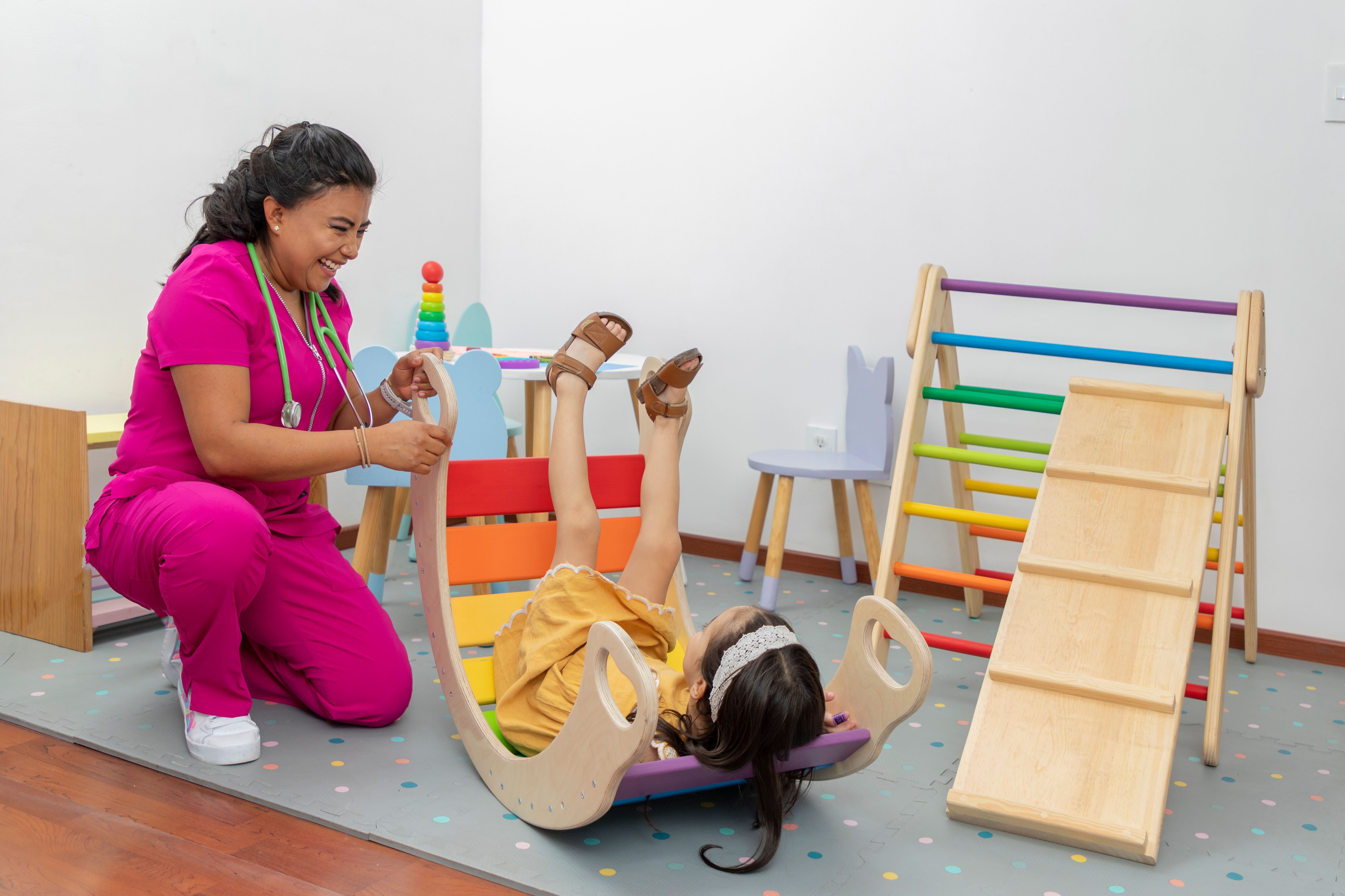 Latina pediatric doctor, laughing while playing with a girl in the play area of her office Latina pediatric doctor, laughing while playing with a girl in the play area of her office