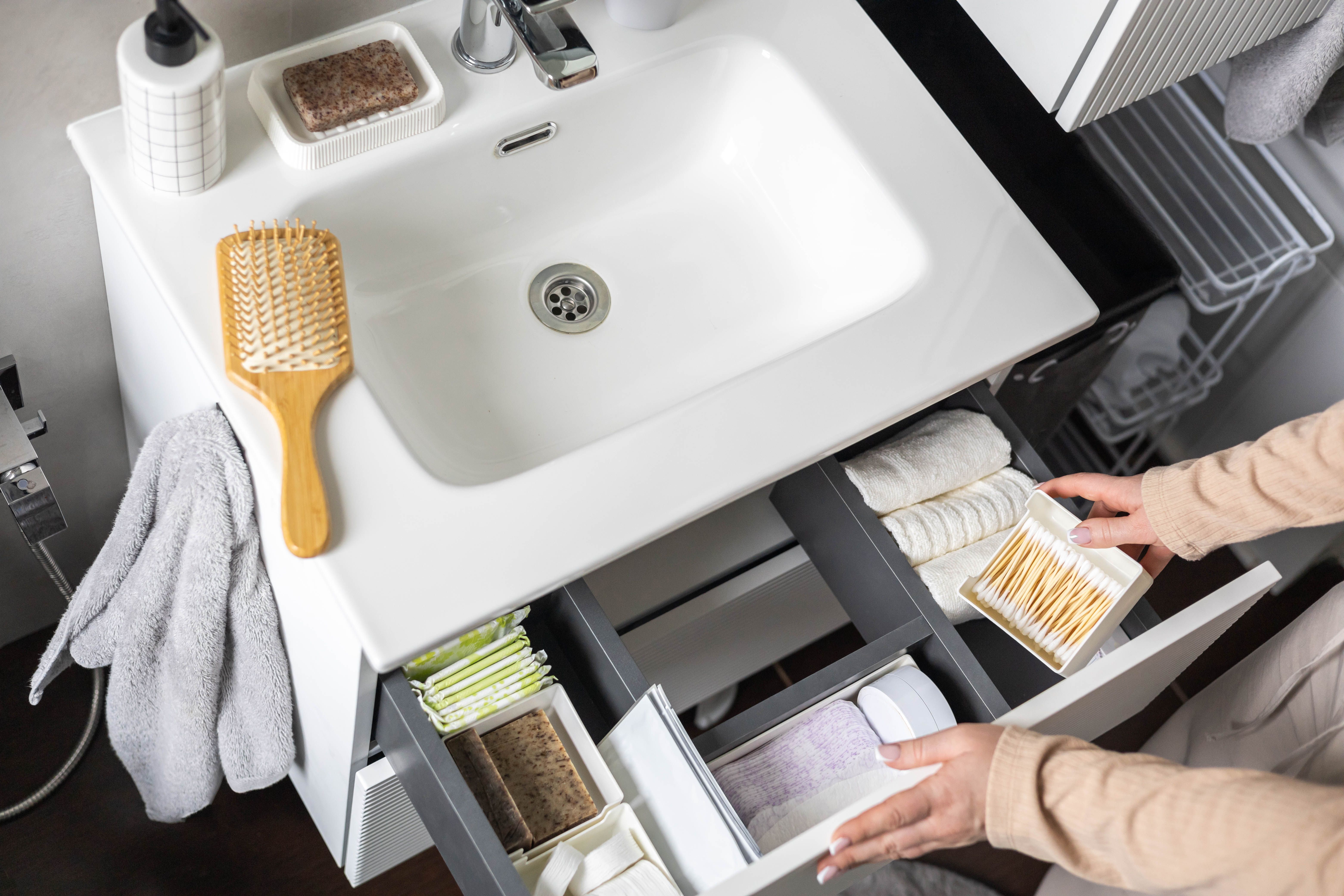 Top view of woman hands neatly organizing bathroom amenities and toiletries in drawer in bathroom.