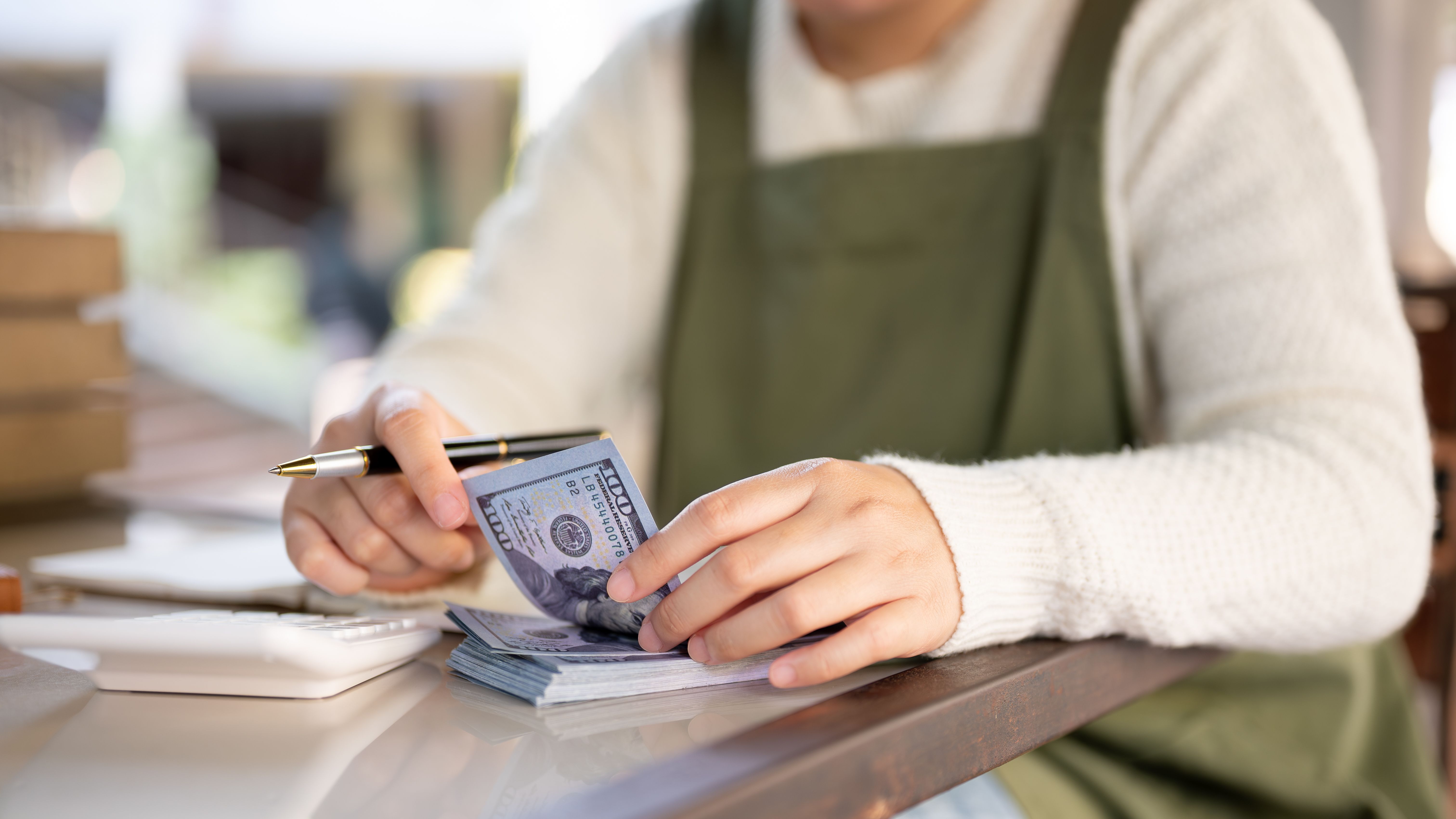 A cropped shot of a female small business owner managing her shop budget, calculating, counting cash A cropped shot of a female small business owner managing her shop budget, calculating, counting cash
