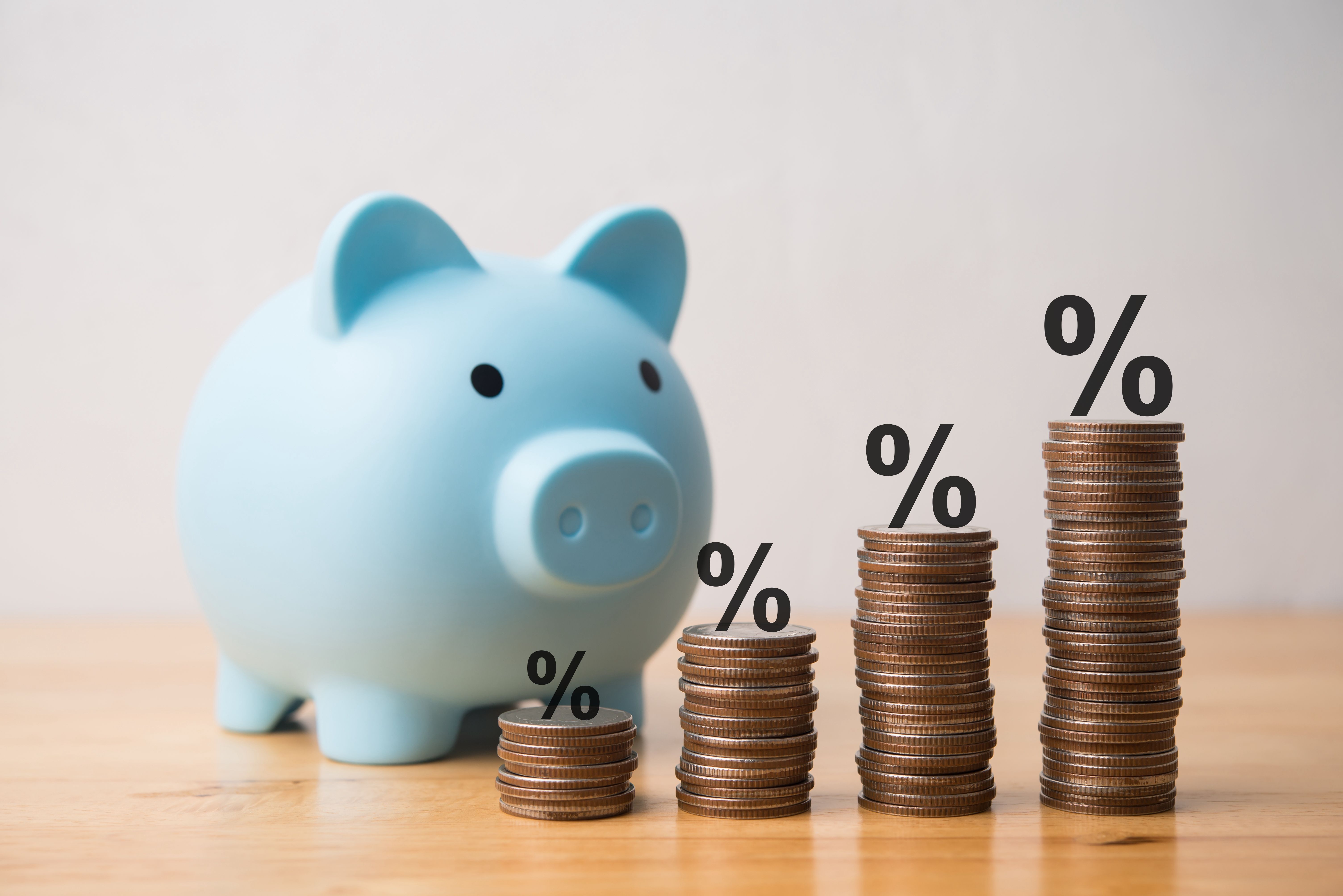 Interest rate or percent sign on growth chart stack coins and blue piggy bank on table.