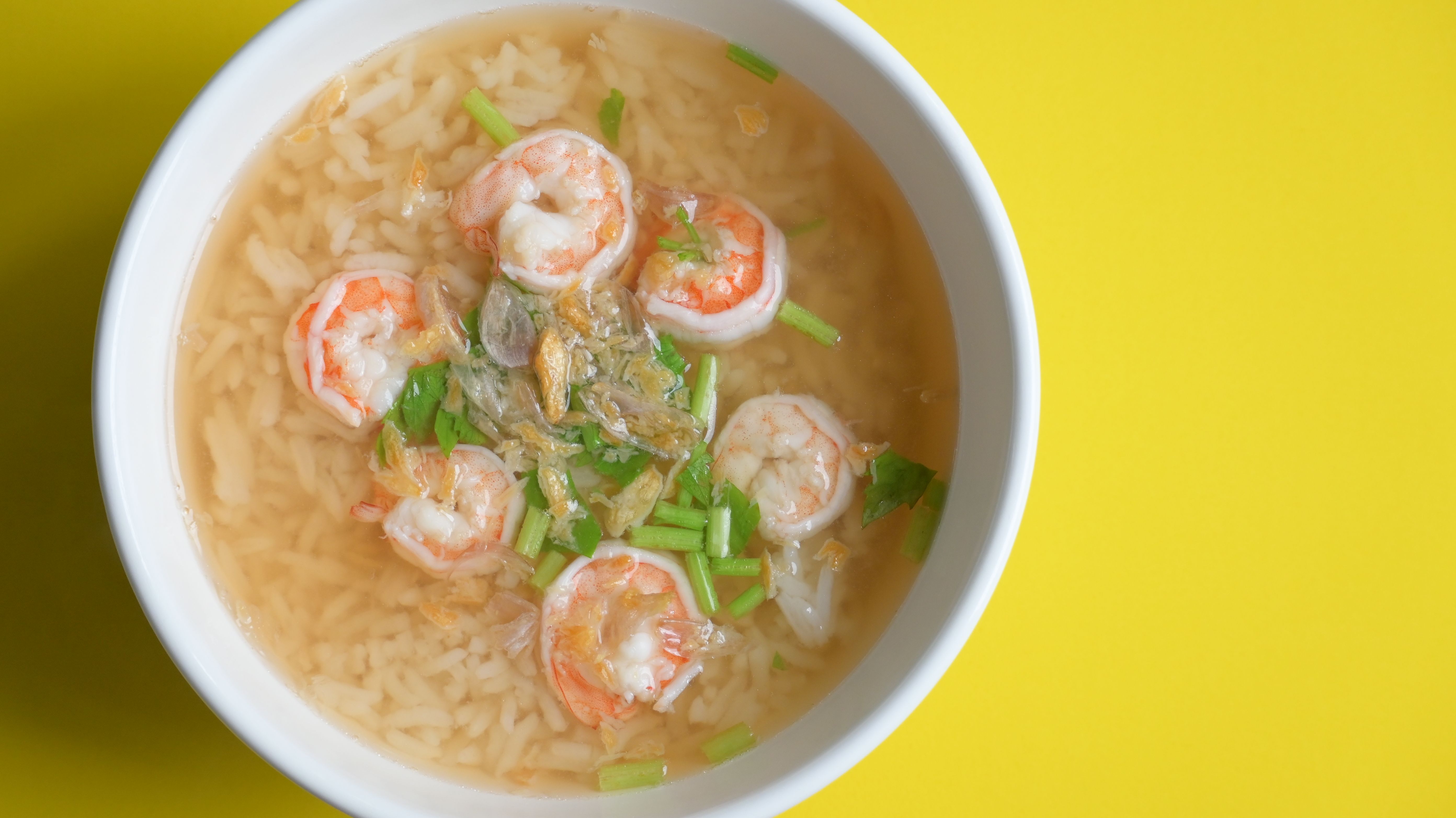 rice soup with shrimp in white bowl on yellow background