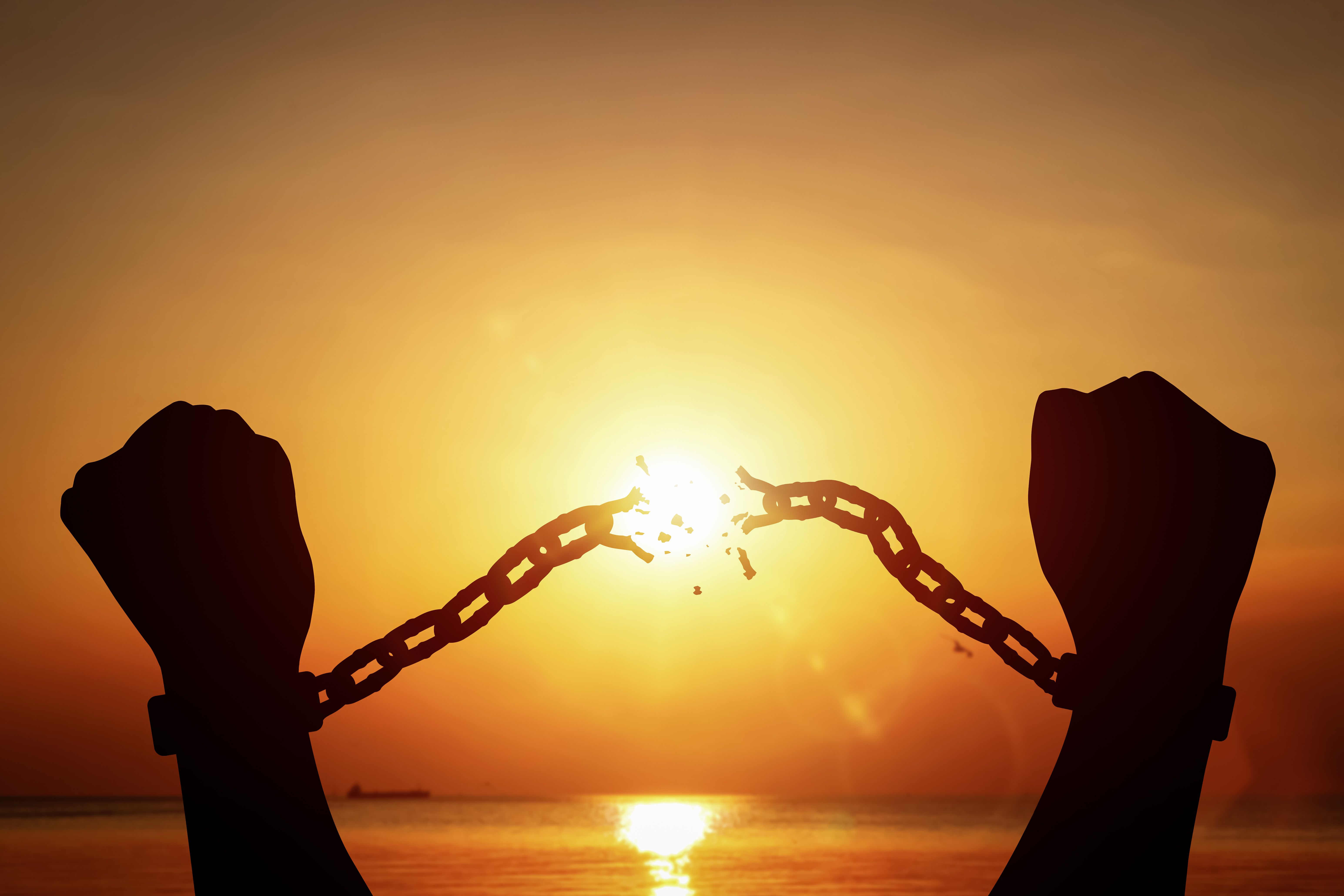 Silhouette of raised hands breaking chains on sunset background. Concept of freedom.