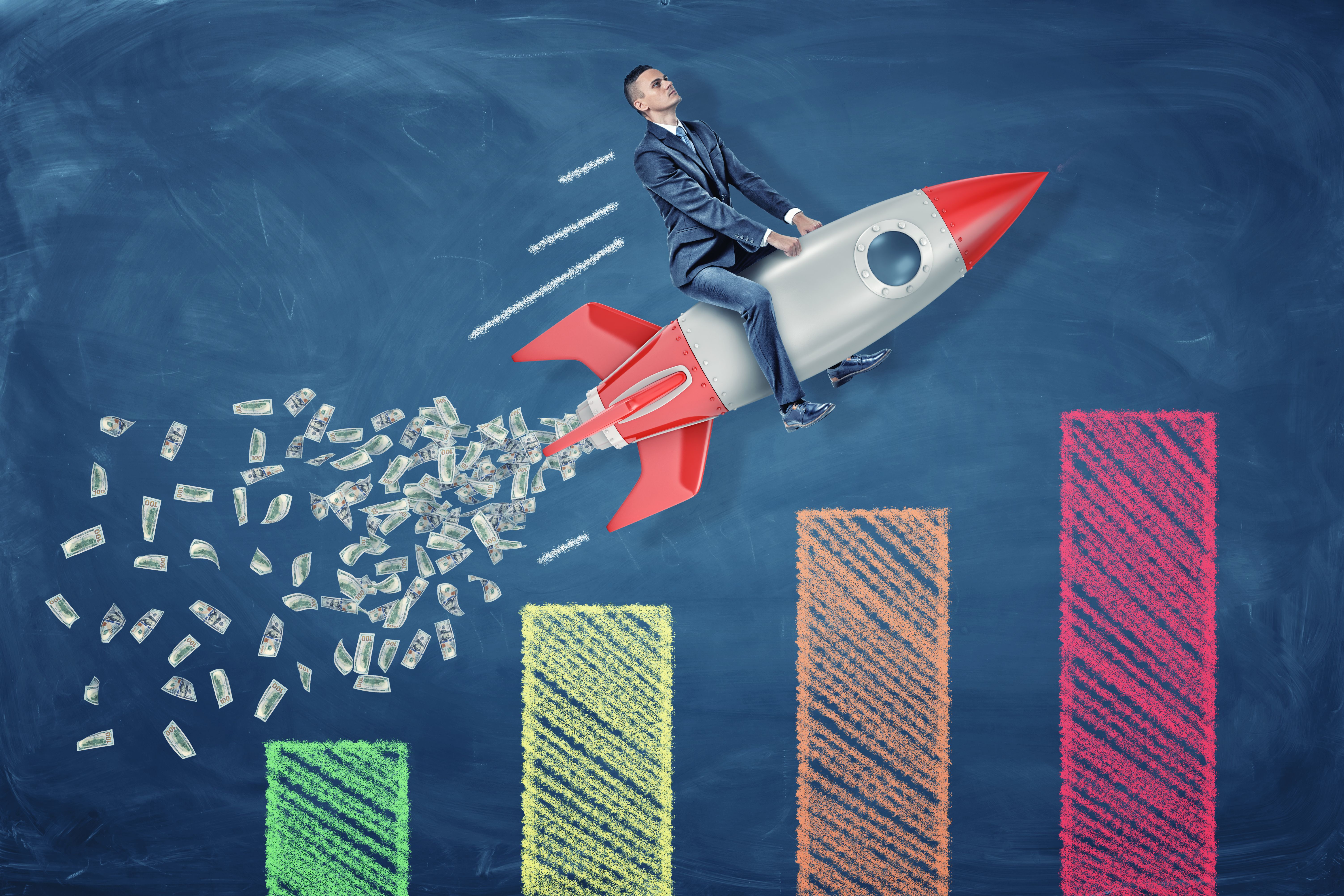 A small businessman rides a rocket leaving a tail of dollar bills over a statistic chart.