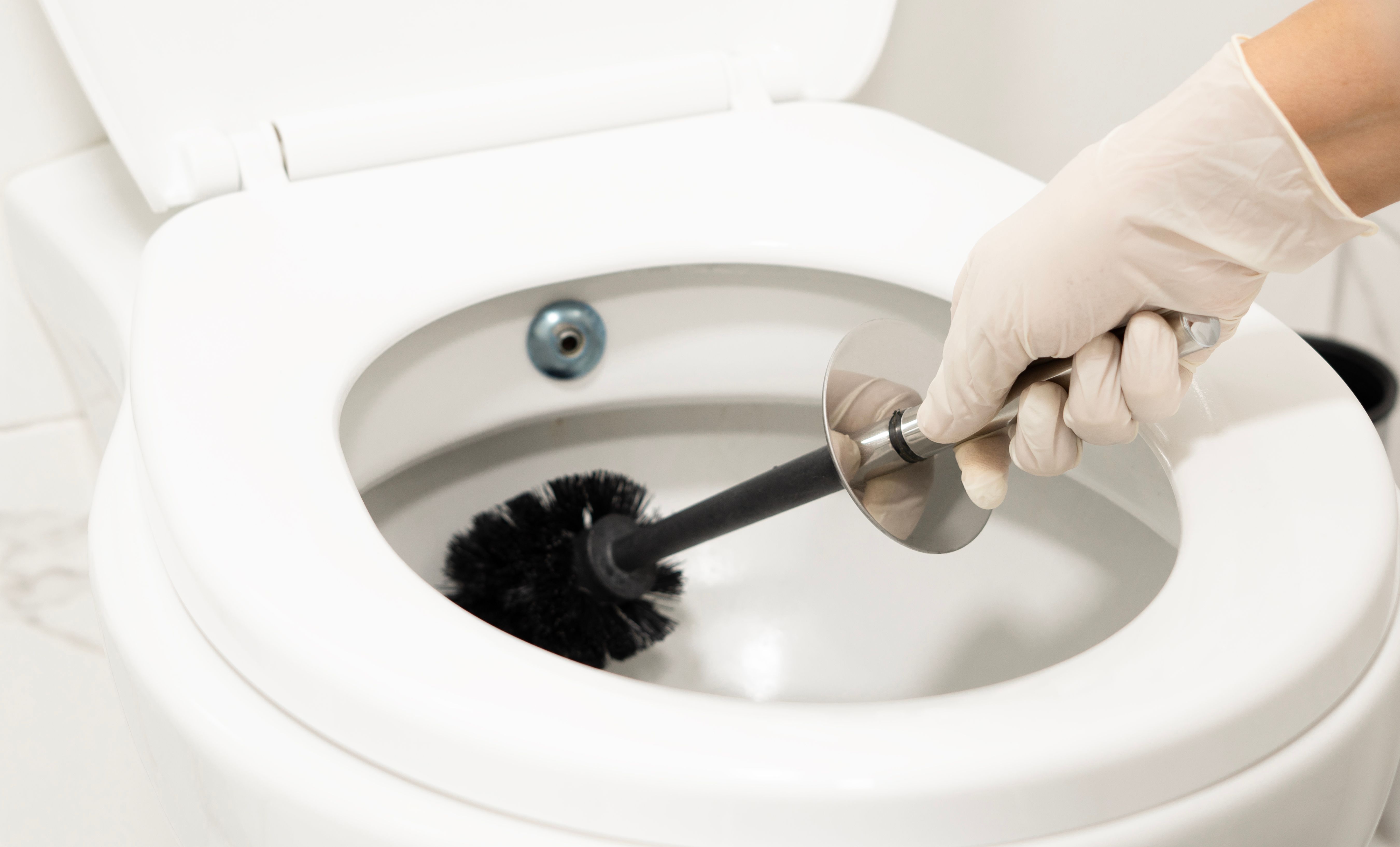 Сlose-up shot of a housekeeper in rubber gloves cleaning a dirty toilet using a special cleaning product and a brush