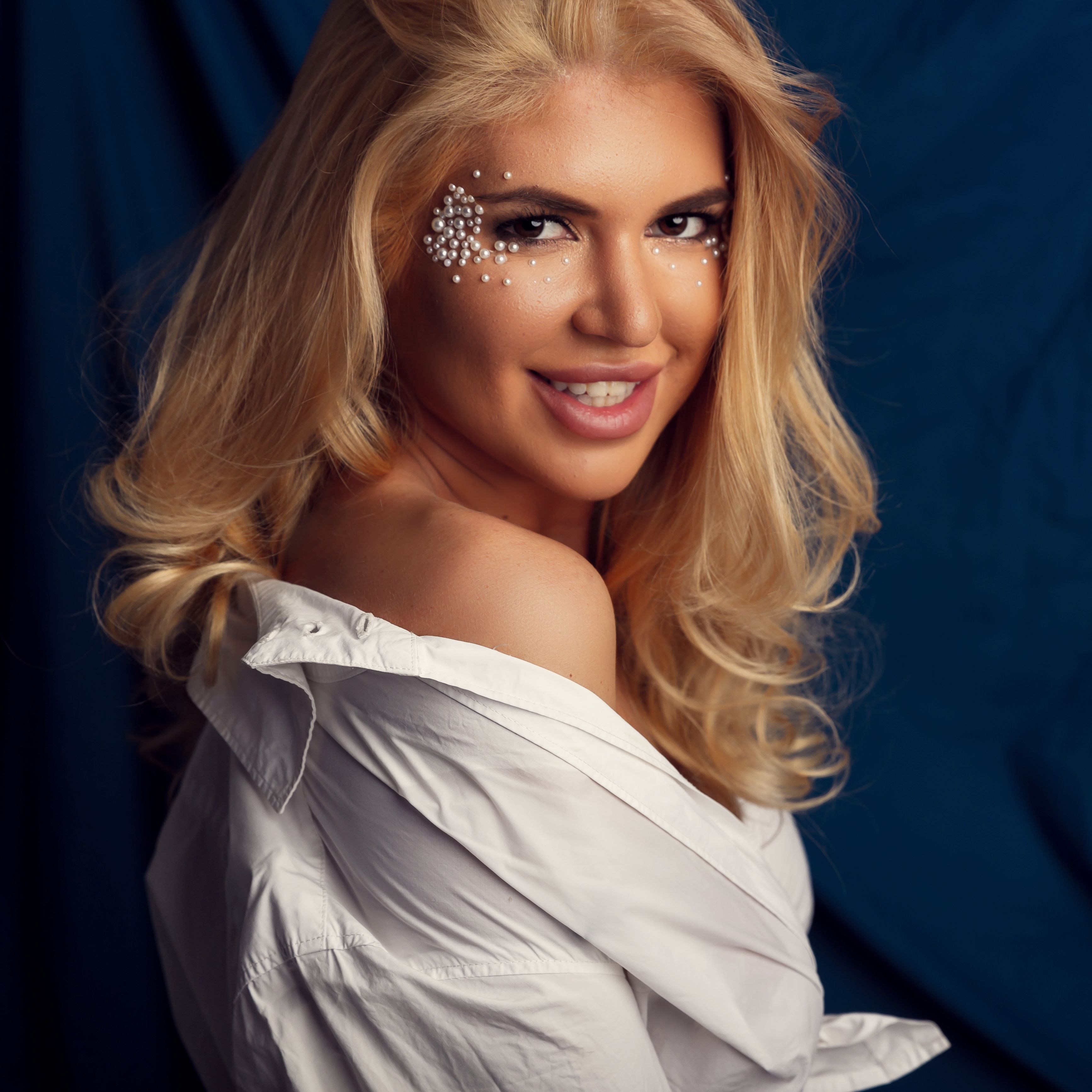 beautiful blonde woman posing in wet white shirt. Girl with perfect slim body on blue silk in studio.