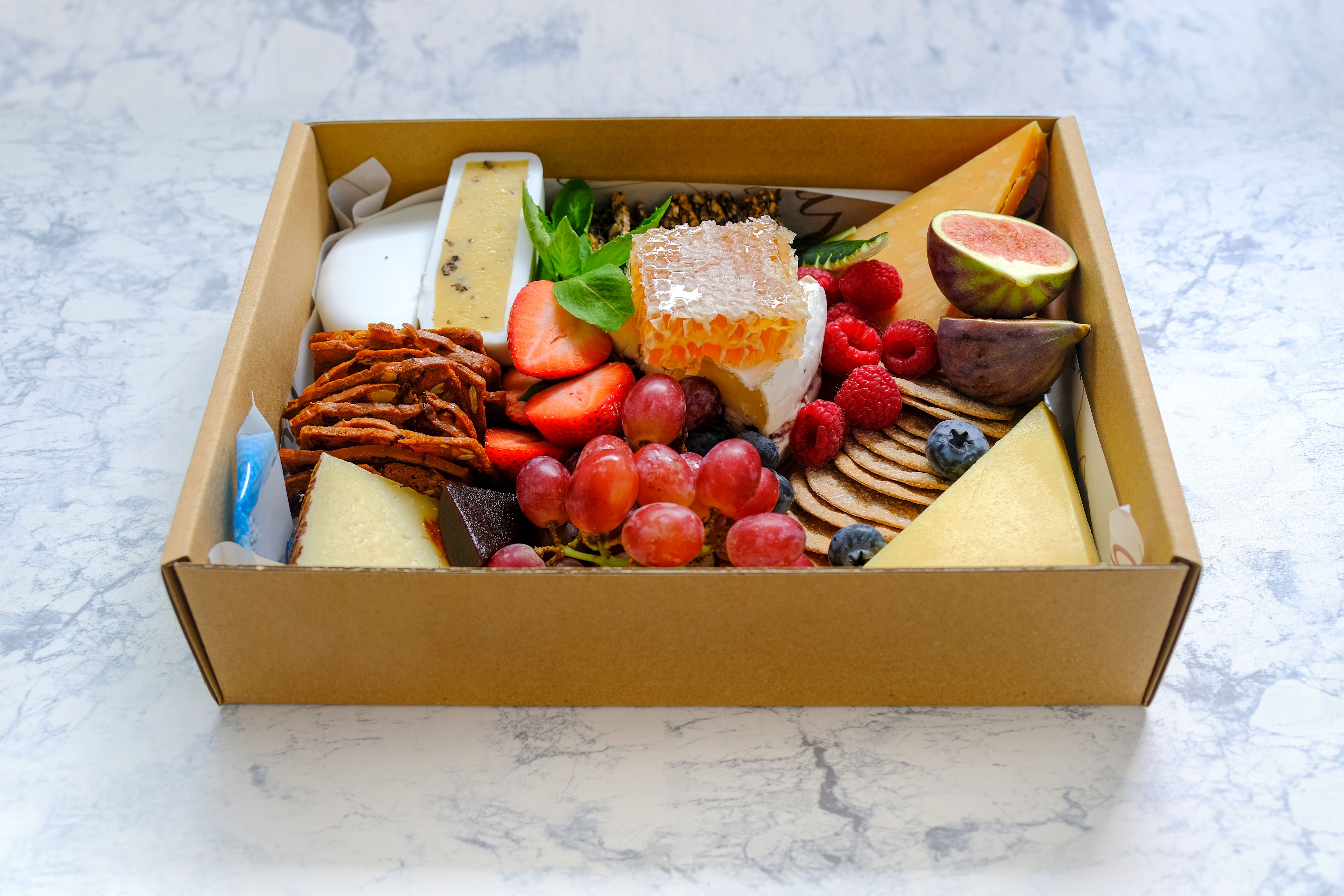 Assortment of fruits cheeses crackers in box isolated on marble pattern table background. Concept for food delivery catering or gift for holiday season or packaging mock up. Top view Selective focus Assortment of fruits cheeses crackers in box isolated on marble pattern table background. Concept for food delivery catering or gift for holiday season or packaging mock up. Top view Selective focus