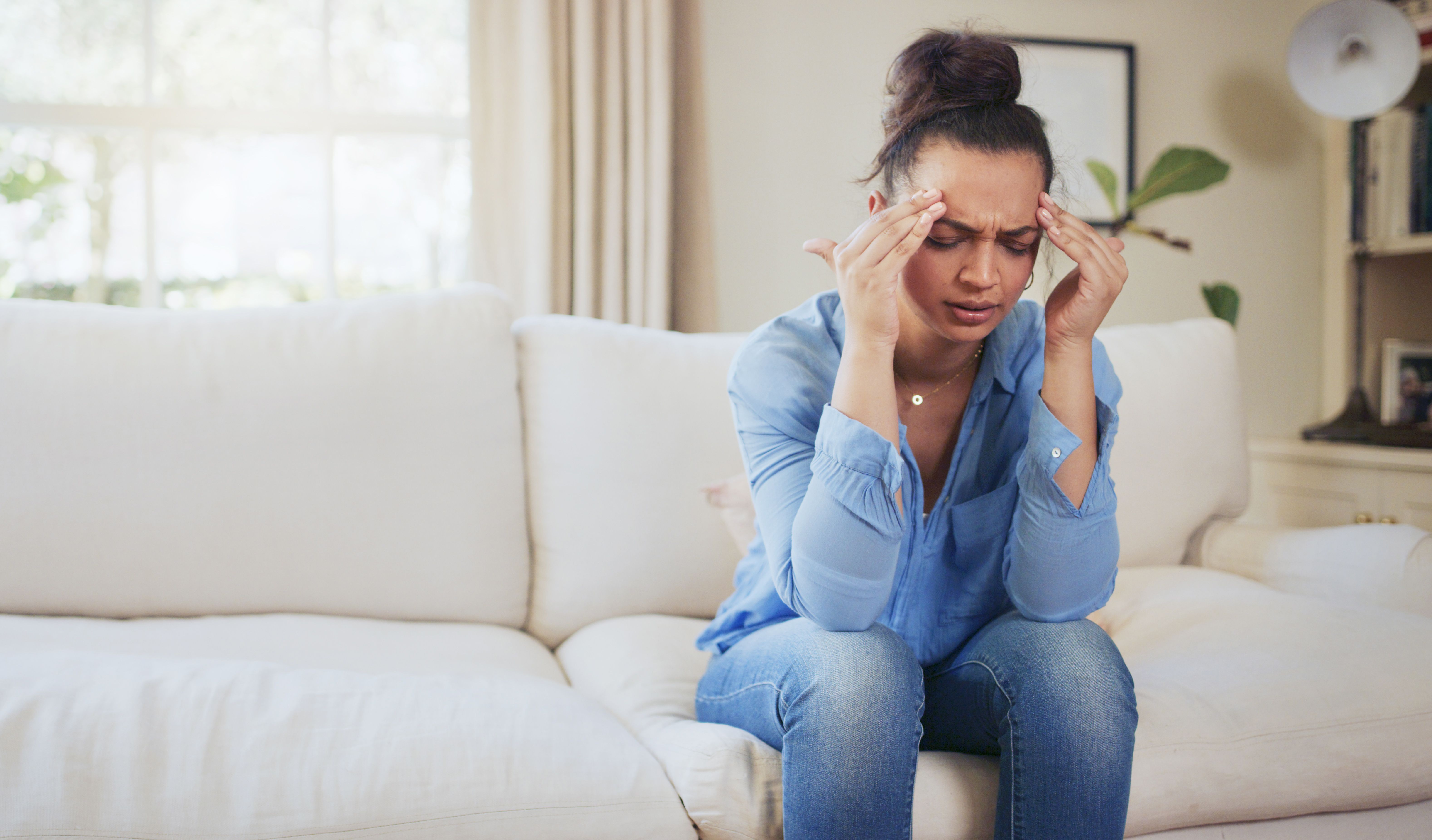Shot of an attractive young woman sitting alone on the sofa at home and feeling stressed