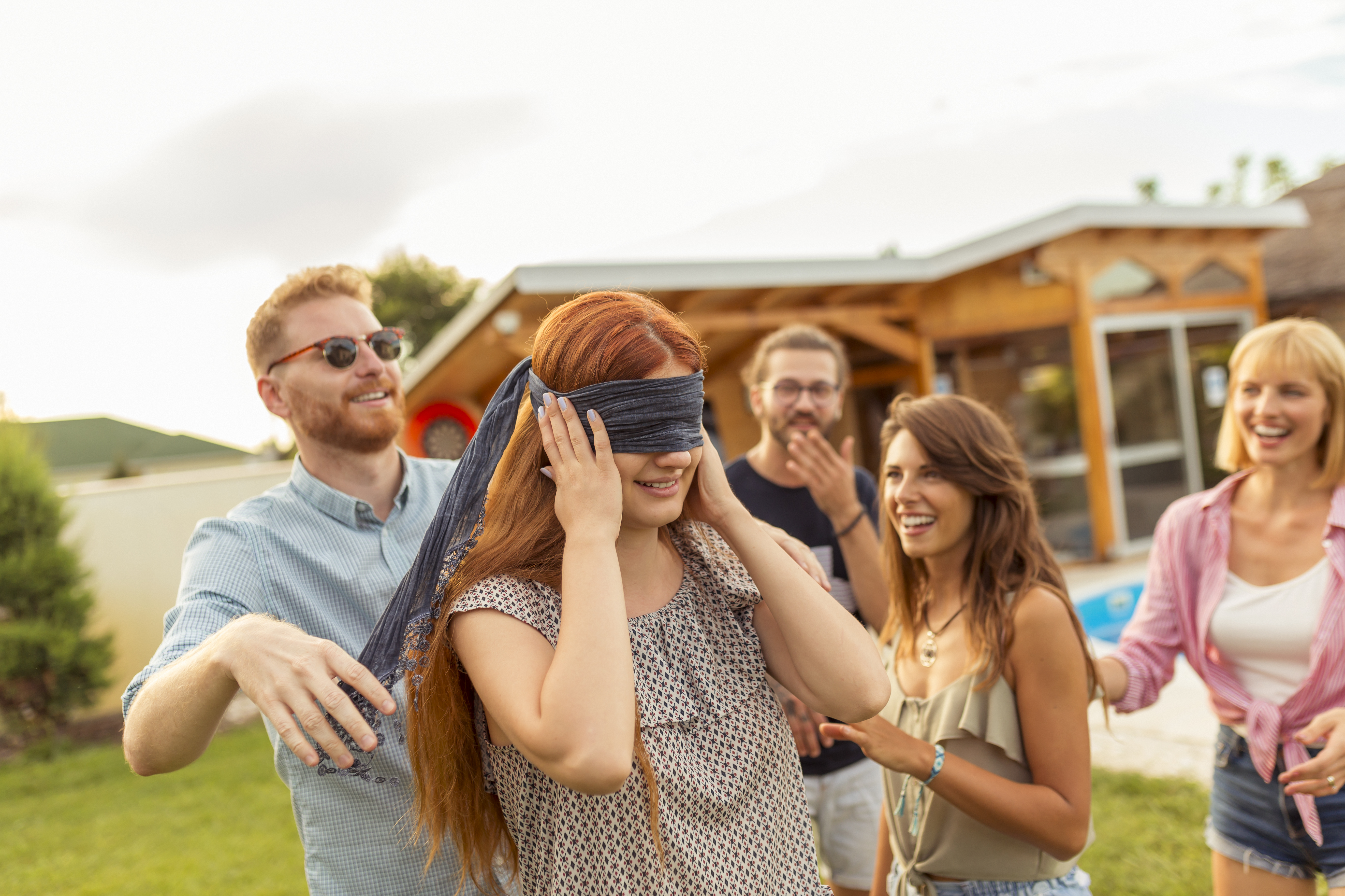 Friends having fun playing blind man's buff while at poolside summertime outdoor party
