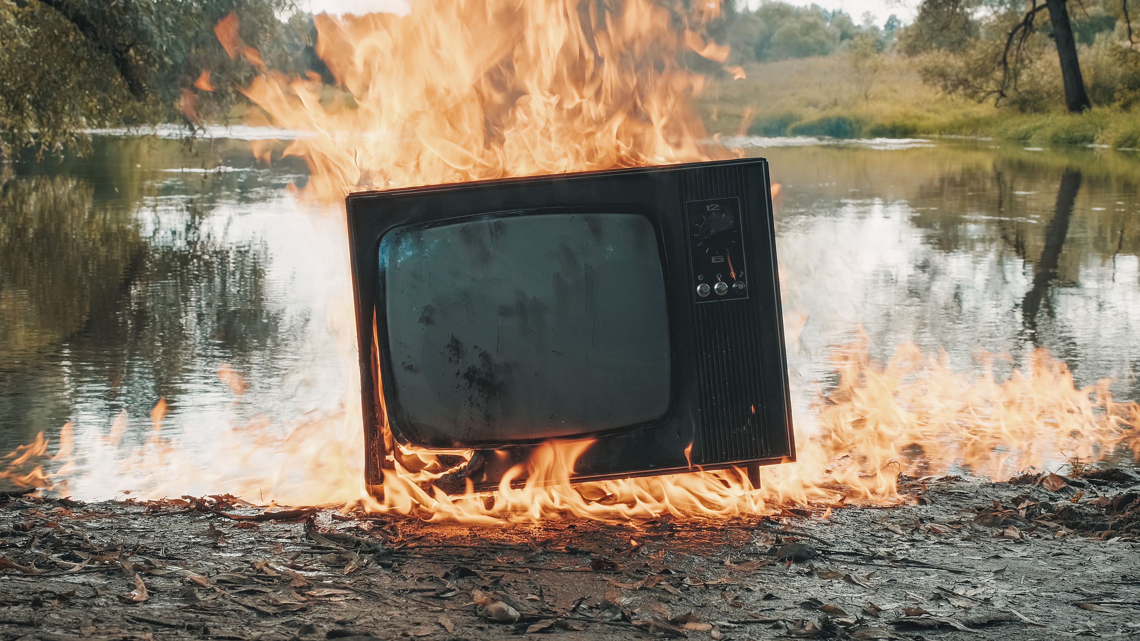 Old vintage TV is burning with fire near the water. The water is also burning