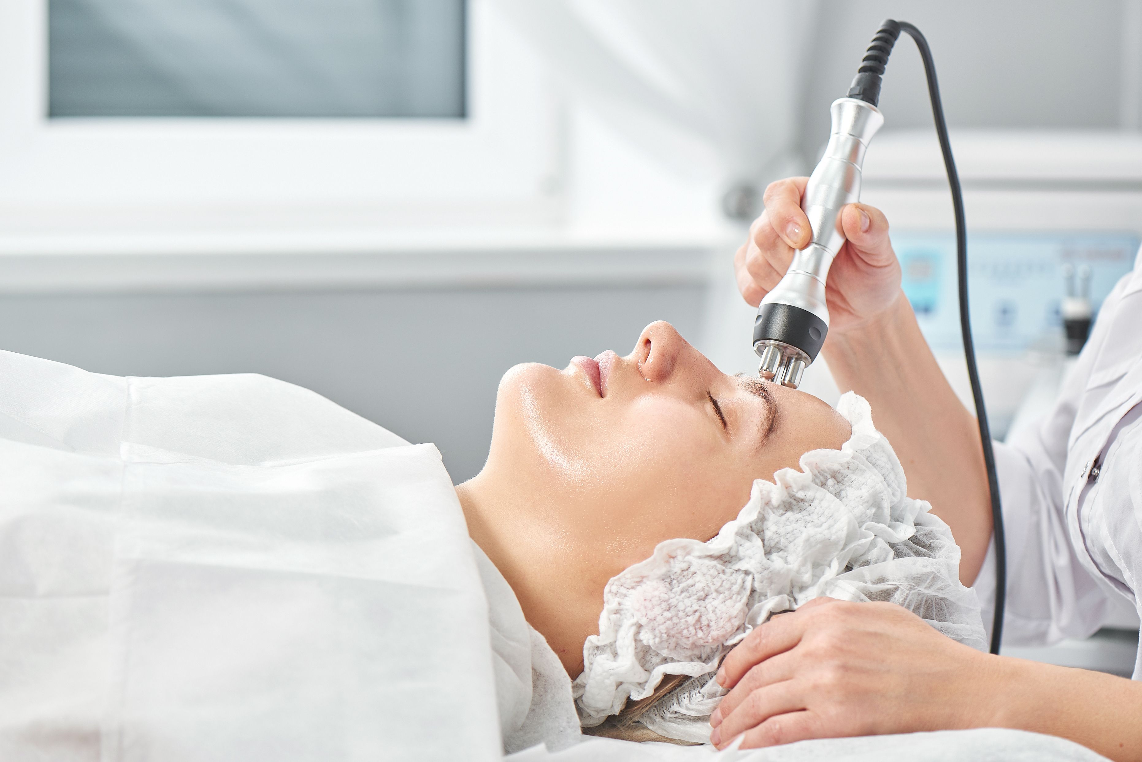 Professional beautician in office conducts session of thermal or radio frequency hardware RF lifting. Tightening and rejuvenation of face skin woman patient close up