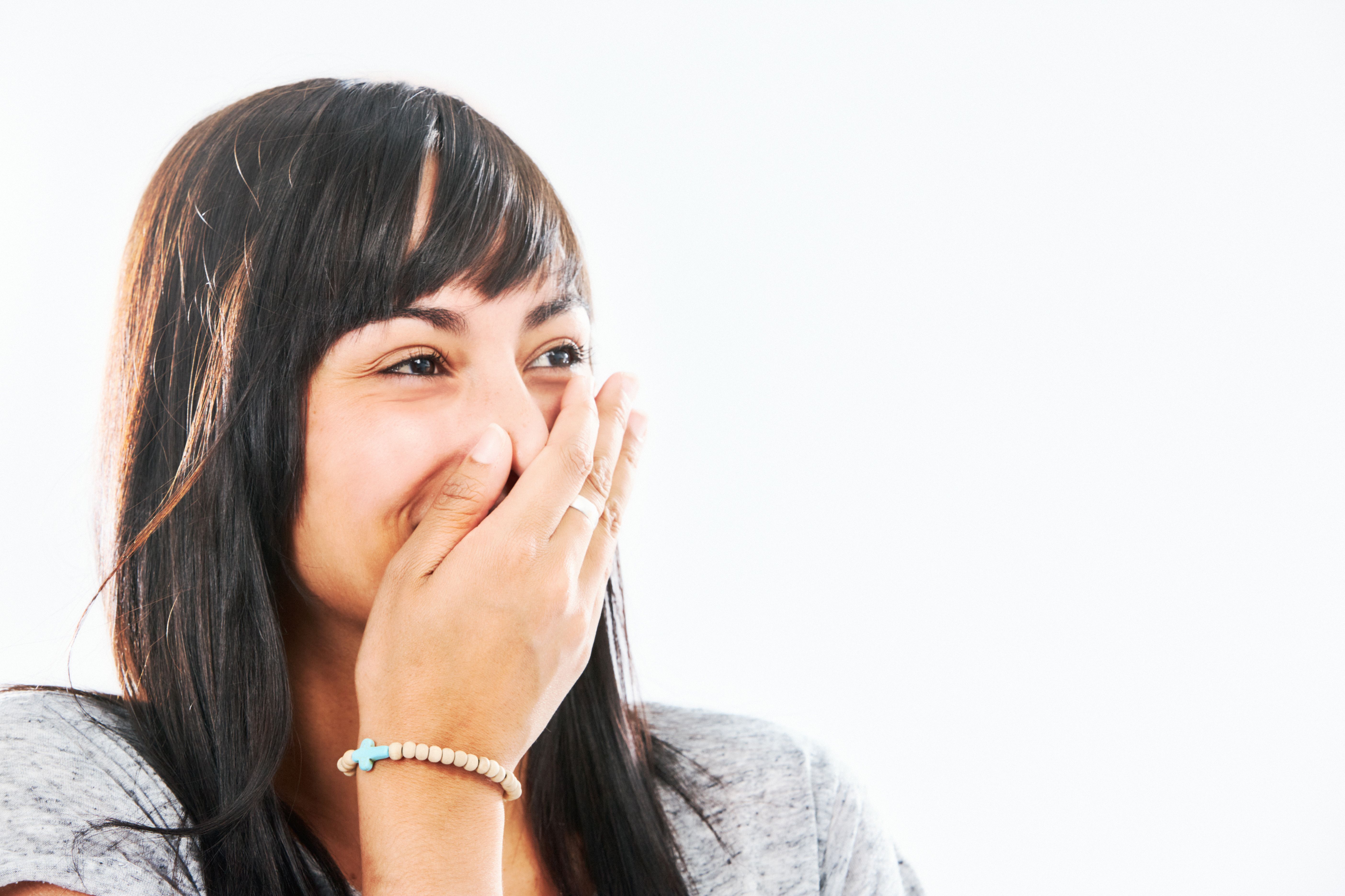 Scandalous! Beautiful young woman with long dark hair covers her mouth as she laughs