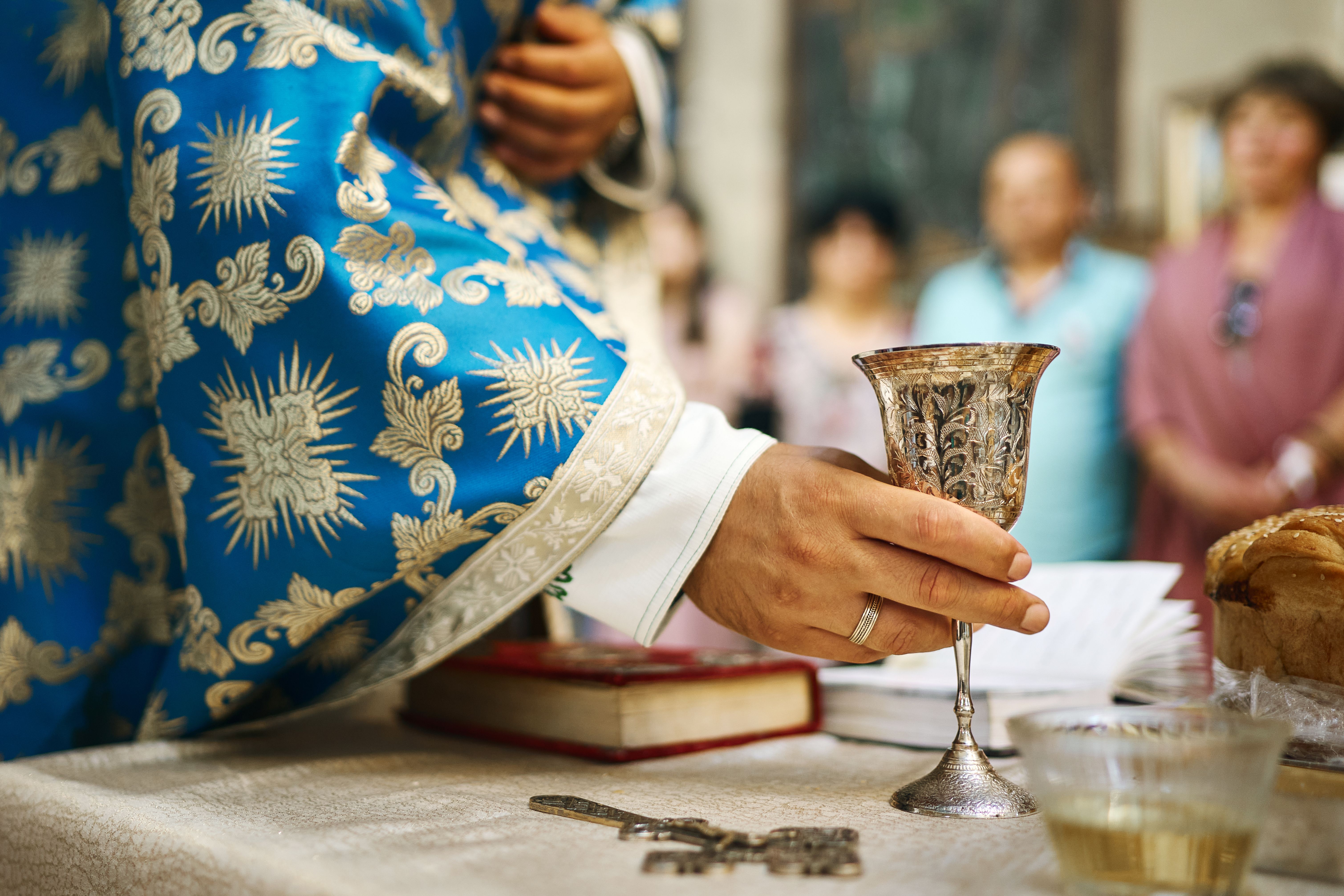 Hands of a priest and a ceremonial wedding cup with wine in wedding ceremony in Orthodox church