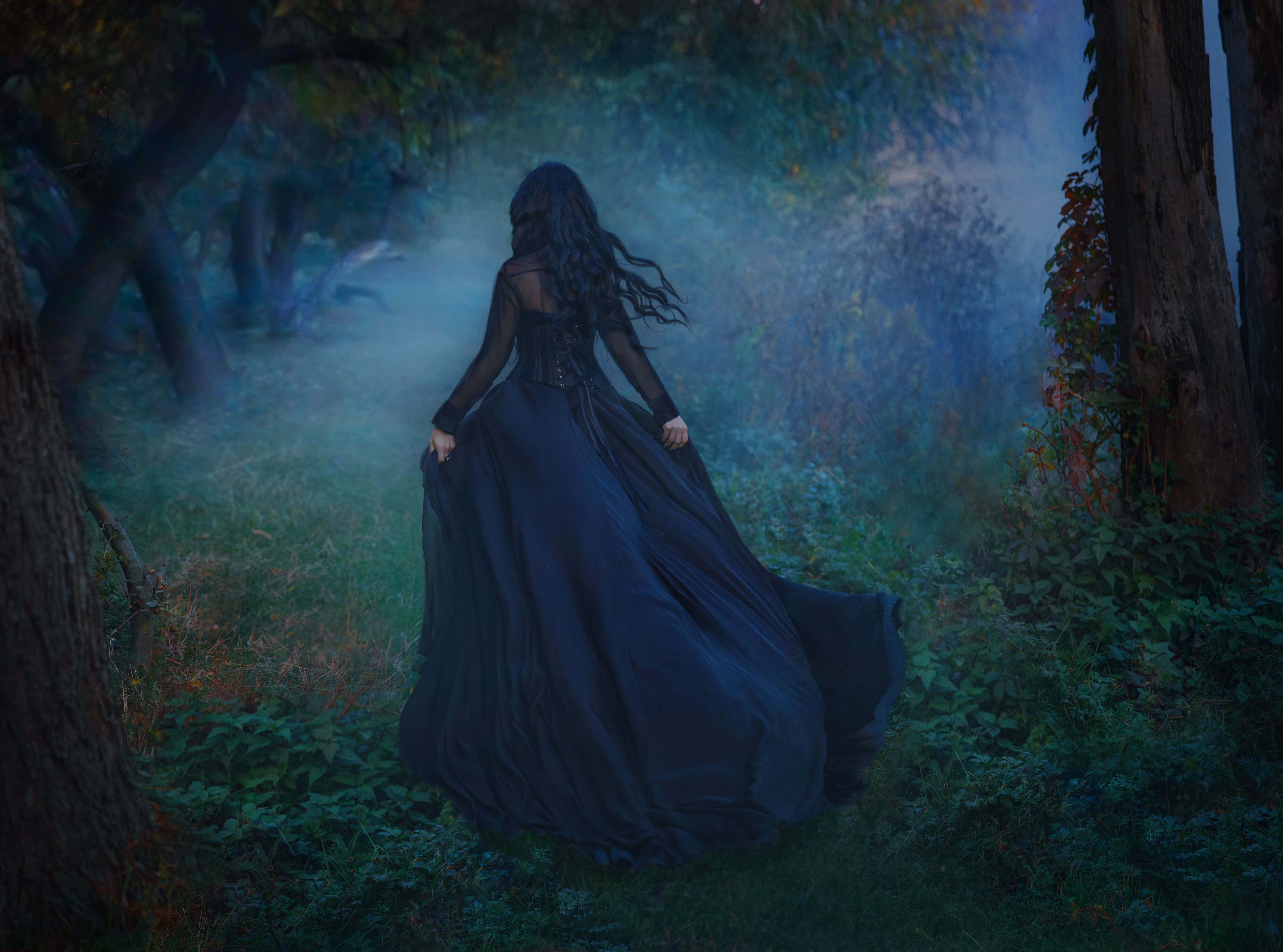 gothic woman queen running in dense forest long dark hair, black dress hem fabric fluttering waving fly in wind motion. Fantasy sexy scared girl. Night nature trees green grass. Happy lady back art