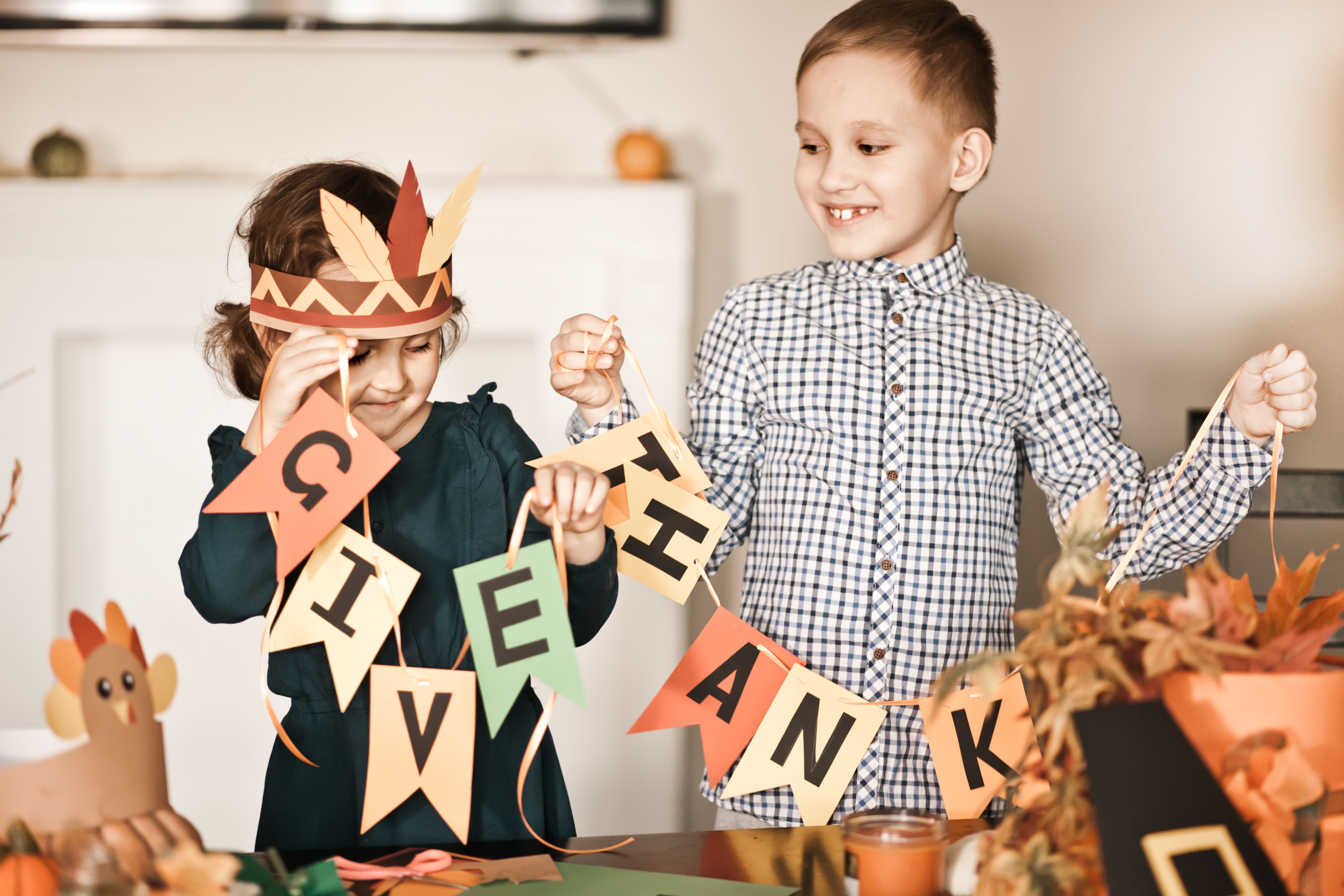 Kid holding paper garland with text Give thanks. Children decorating living room for celebrating Thanksgiving day. Kid holding paper garland with text Give thanks. Children decorating living room for celebrating Thanksgiving day.