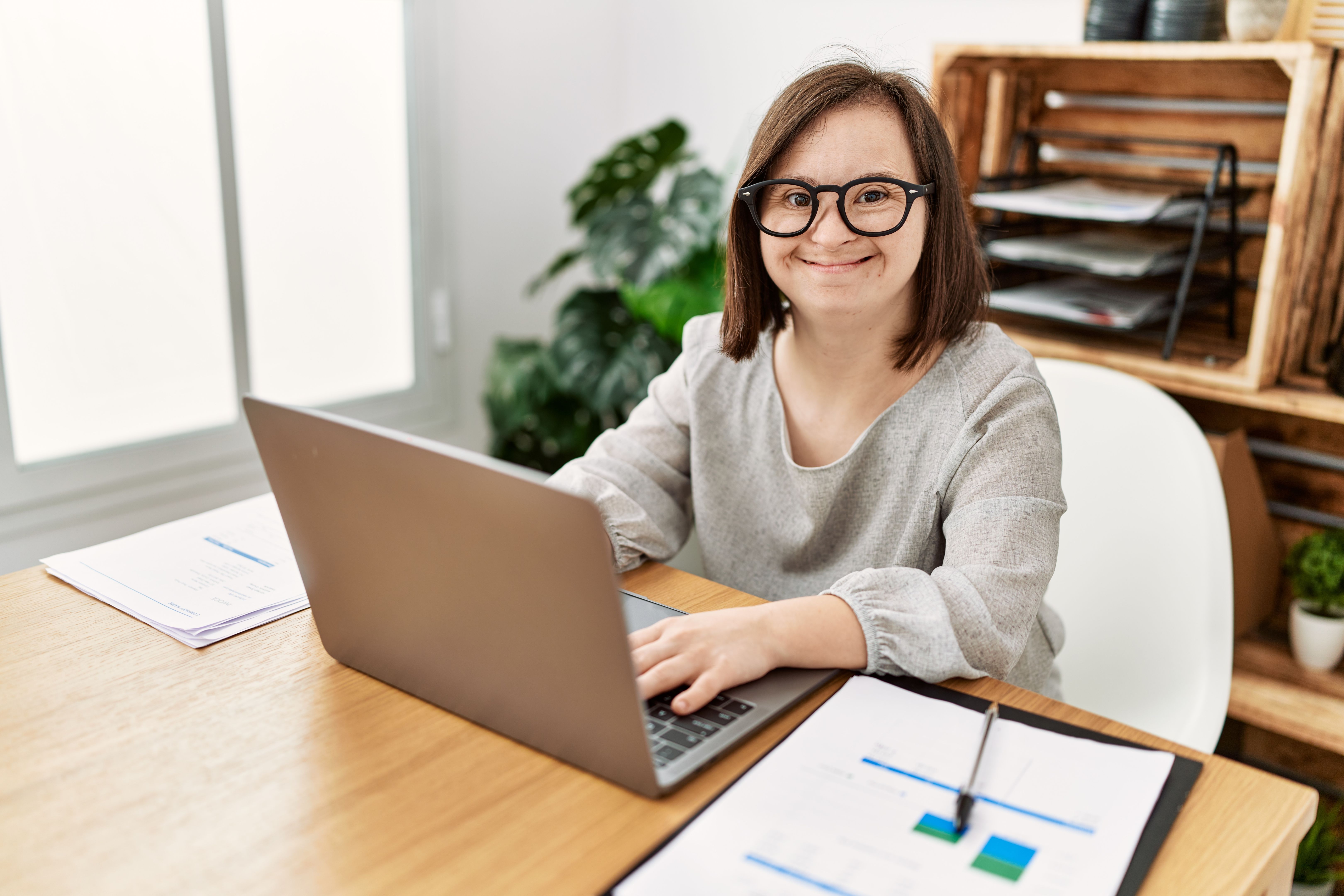 Brunette woman with down syndrome working using laptop at business office