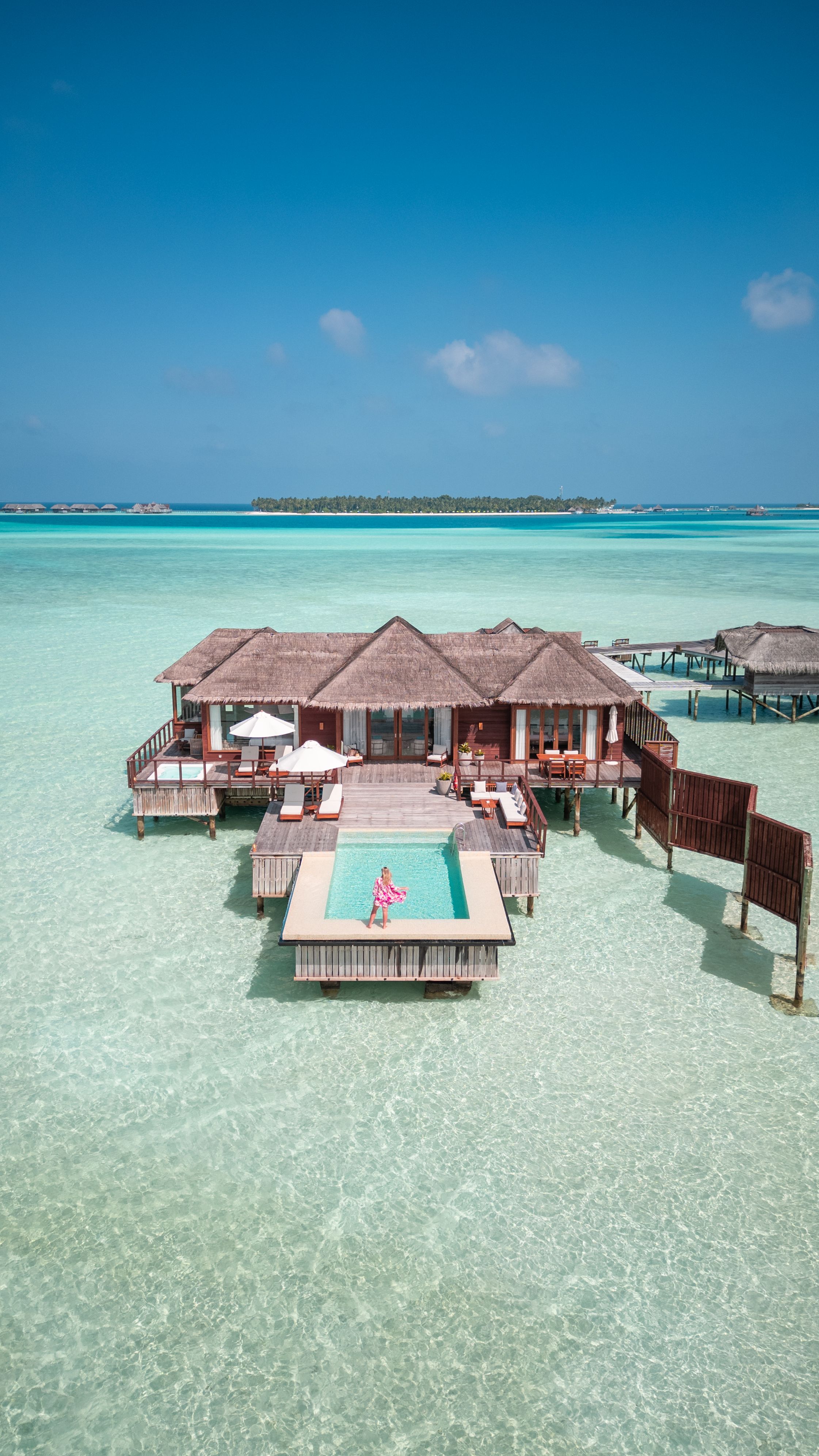 Aerial drone view of Maldives overwater villa jetty bungalow with swimming pool in tropical island resort lagoon and woman enjoying vacation